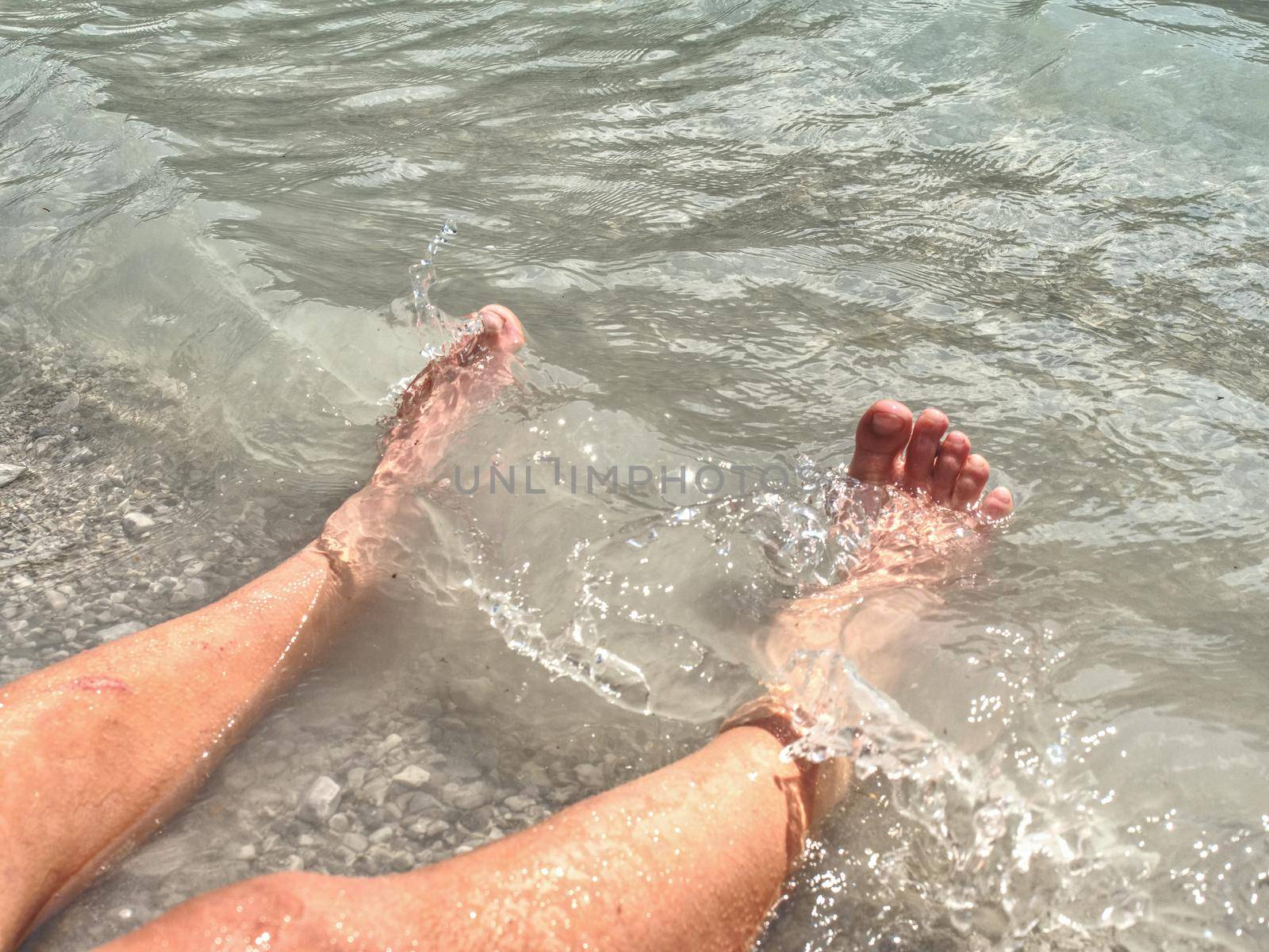Naked legs along wave of lake water and rough white stony sand on the beach. Carefree and relaxing attitude