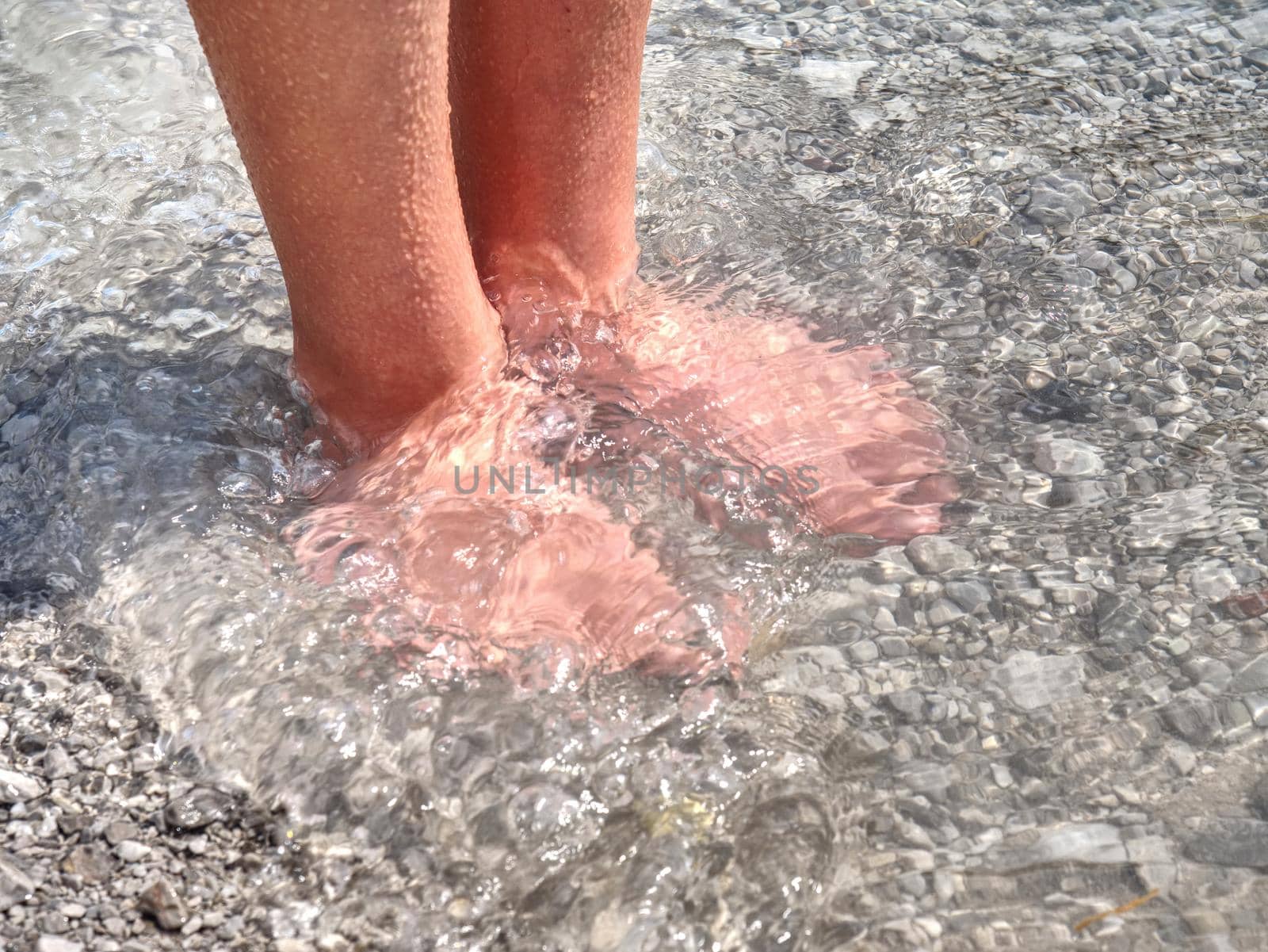Hairy strong male legs are cooling in cold water of mountain lake. Green blue cold water of kaje in Dolomiti.