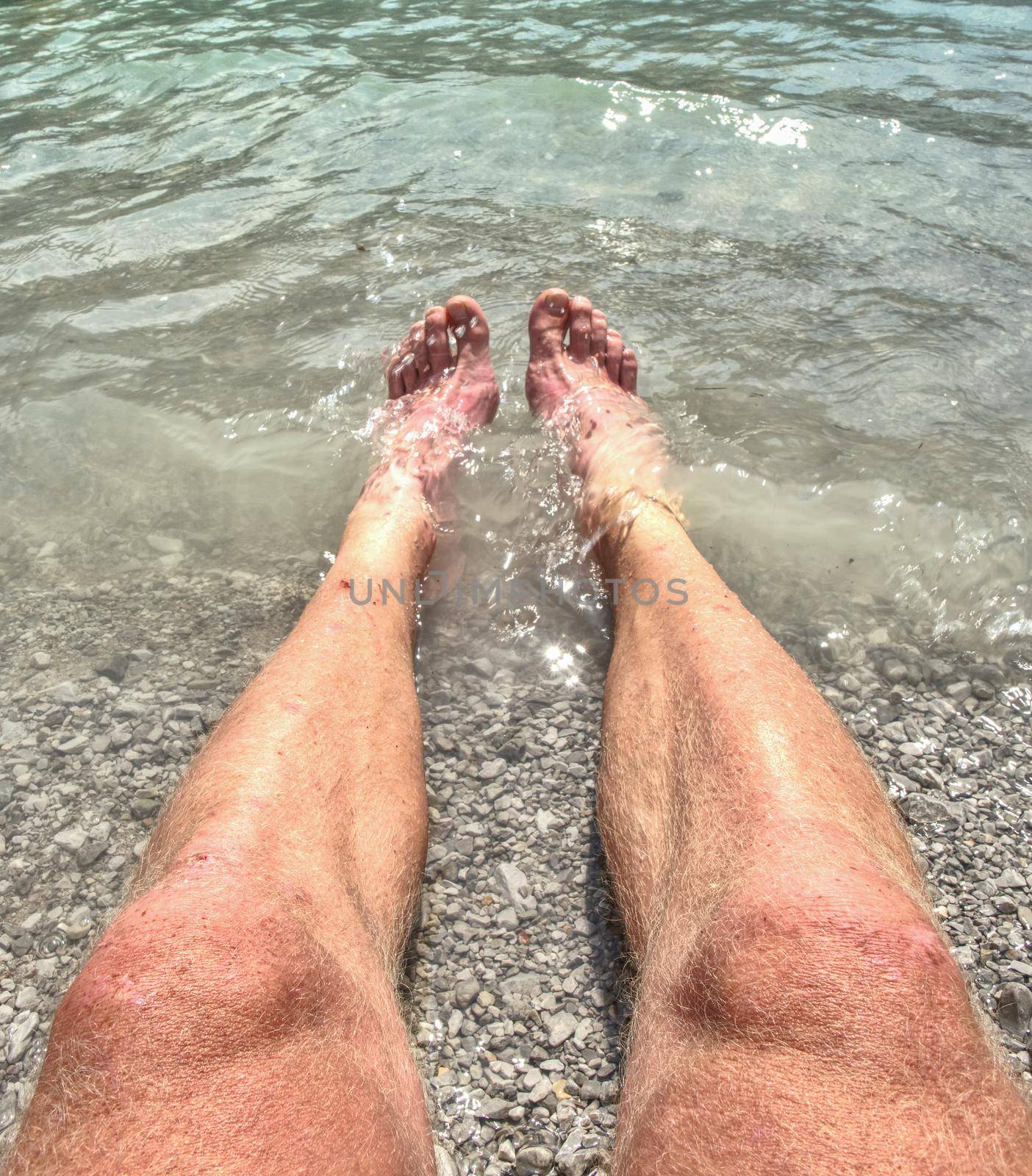 Legs and feet on stones of the beach with the lake or sea water. by rdonar2