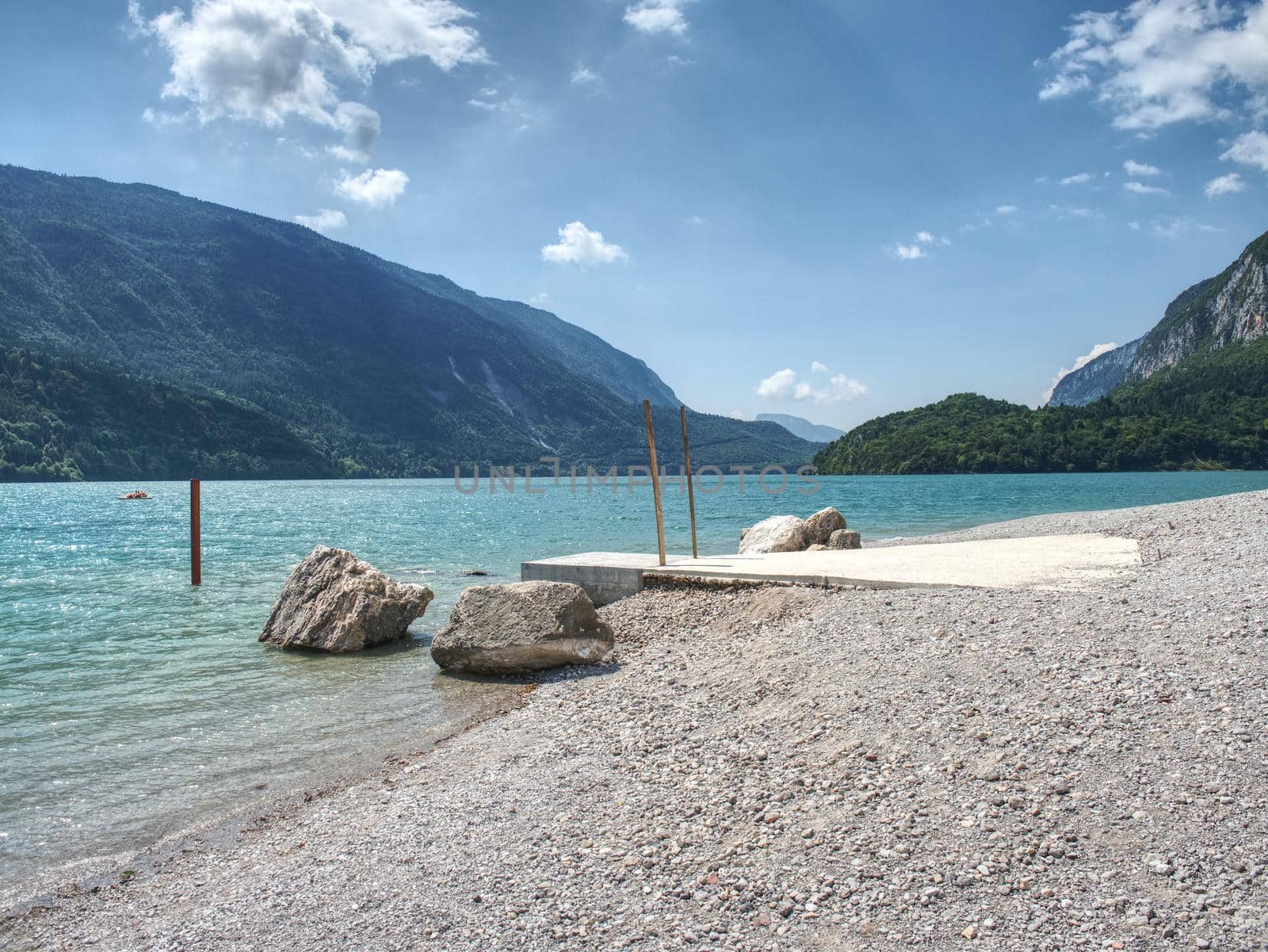 Stones stack on shore of blue green water of mountain lake. Blue mountains in water level mirror.