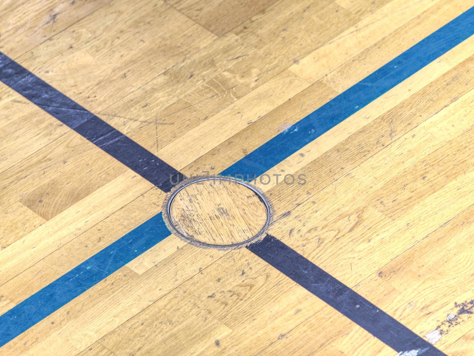 Circle cover plug for sport equipment in floor of school gym. Painted lines on wooden floor of sporting hall with sratched surface.