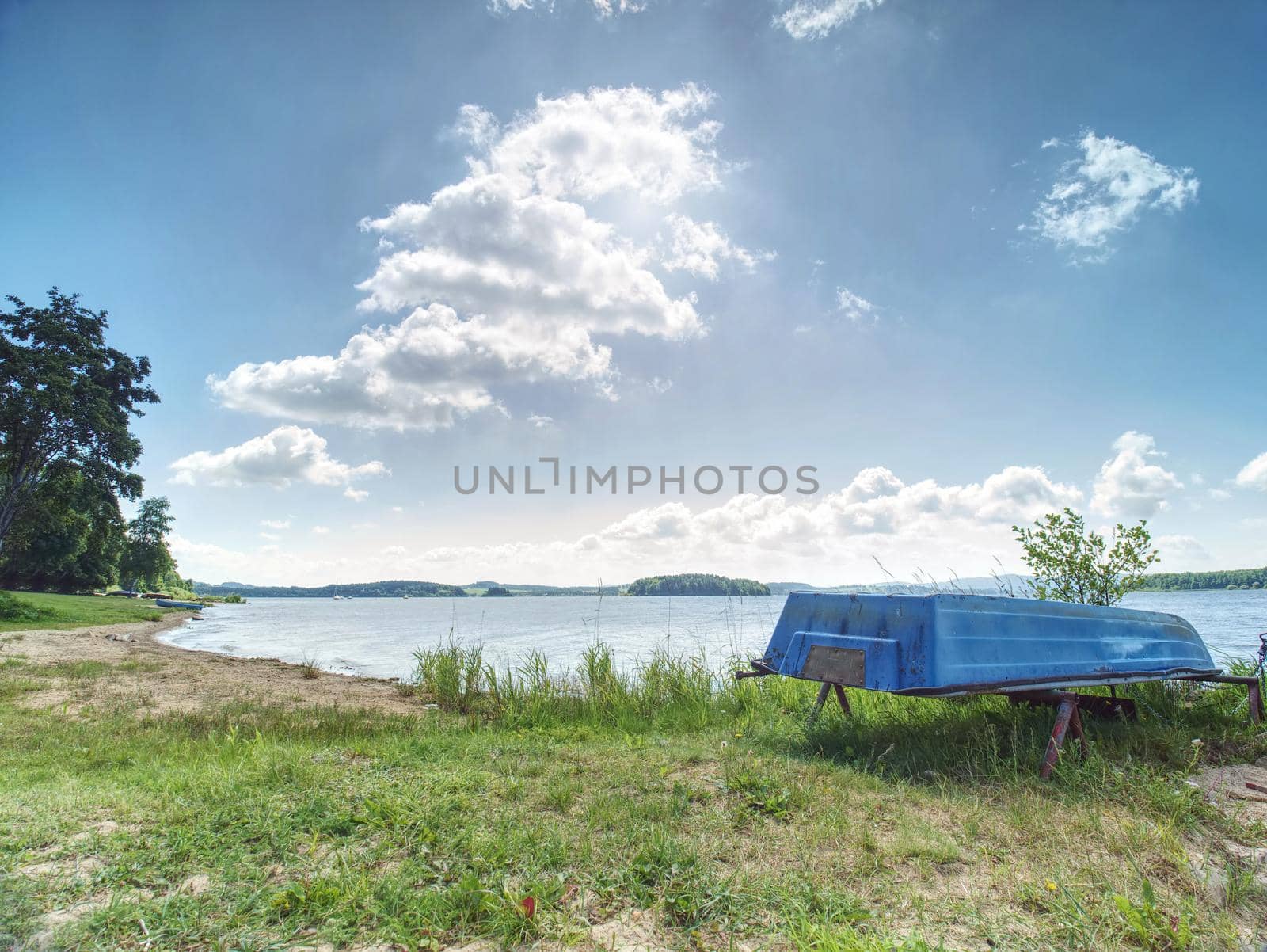 Old fishing rowing boat stacked upside down under tree at large smooth water level of Lipno lake. Calm windless evening at popular holiday destination.