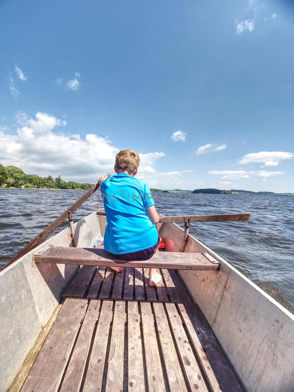 Boy in blue with life jackets at legs floats on vessel boat and hard woarking. Young man in metal  boat sail on lake water