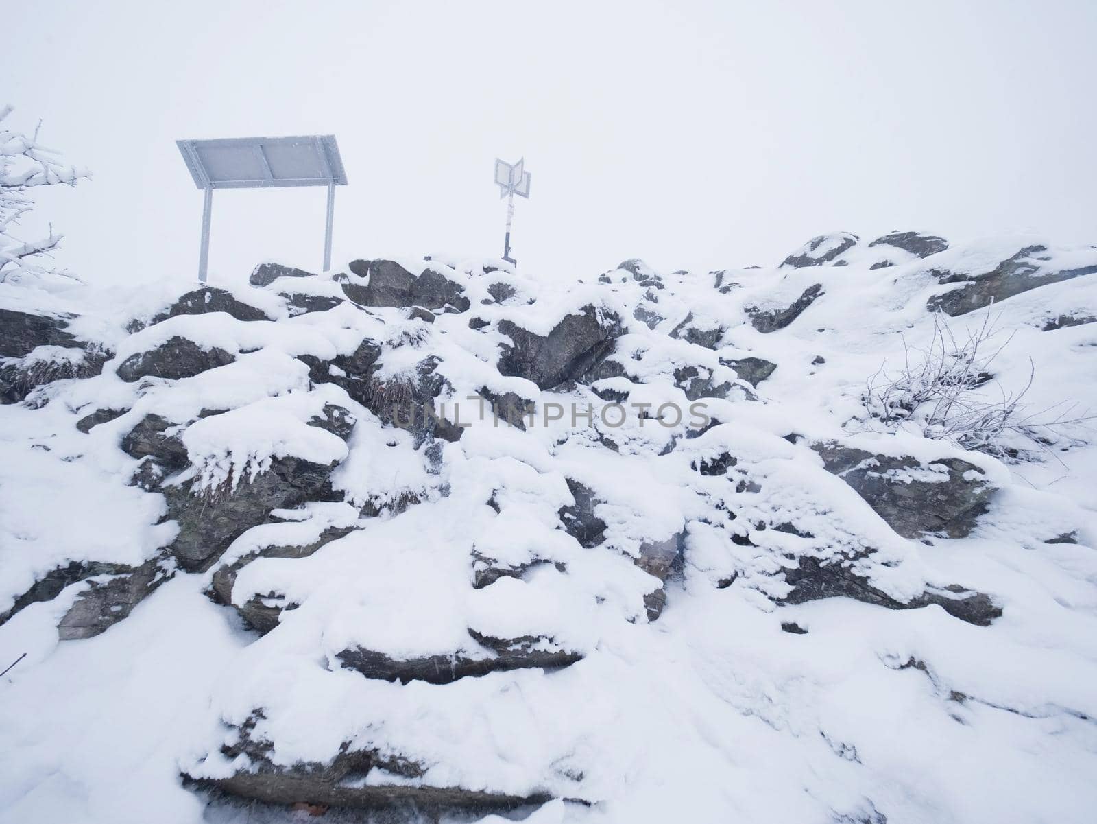 Close up to rocky terrain with fresh powder snow, landscape hidden in heavy fog. Misty winter day