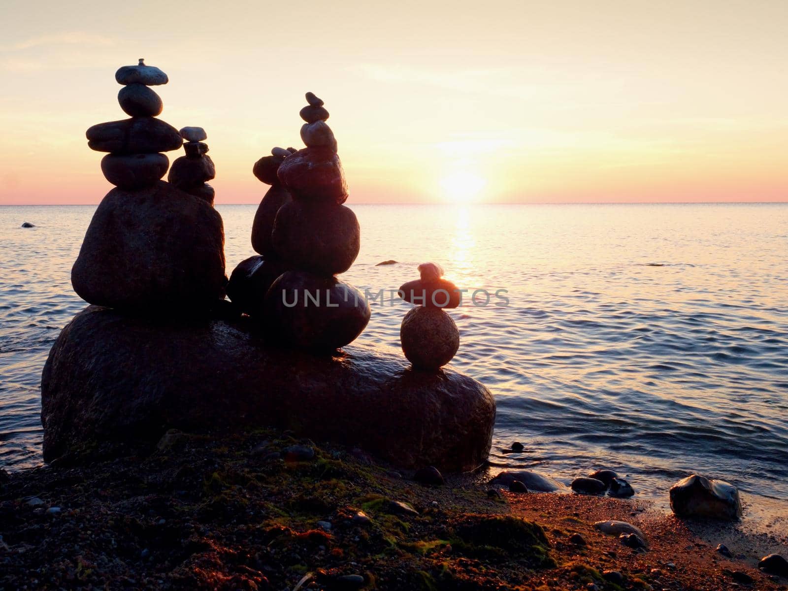 Balanced stone pyramid on sea shore, romantic sunset at horizon by rdonar2