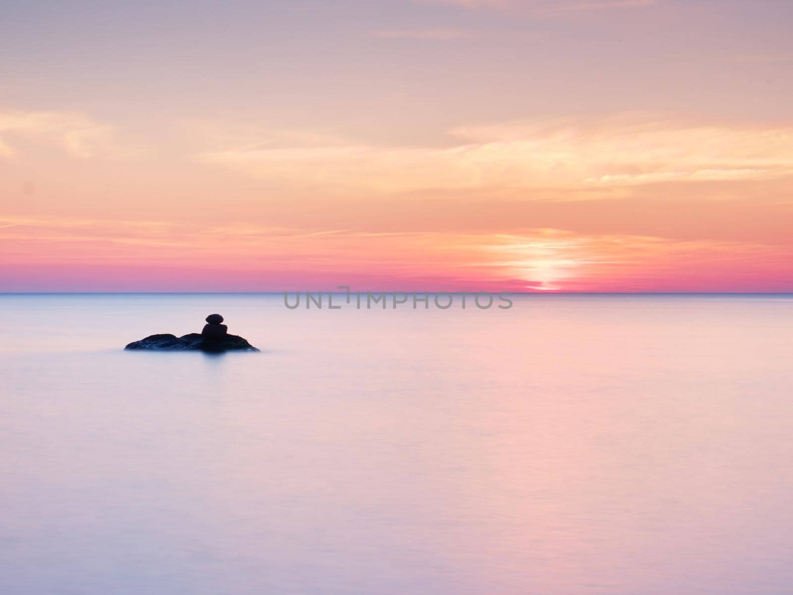 Romantic morning at sea. Big boulders sticking out from smooth wavy sea. Pink horizon with first hot sun rays.