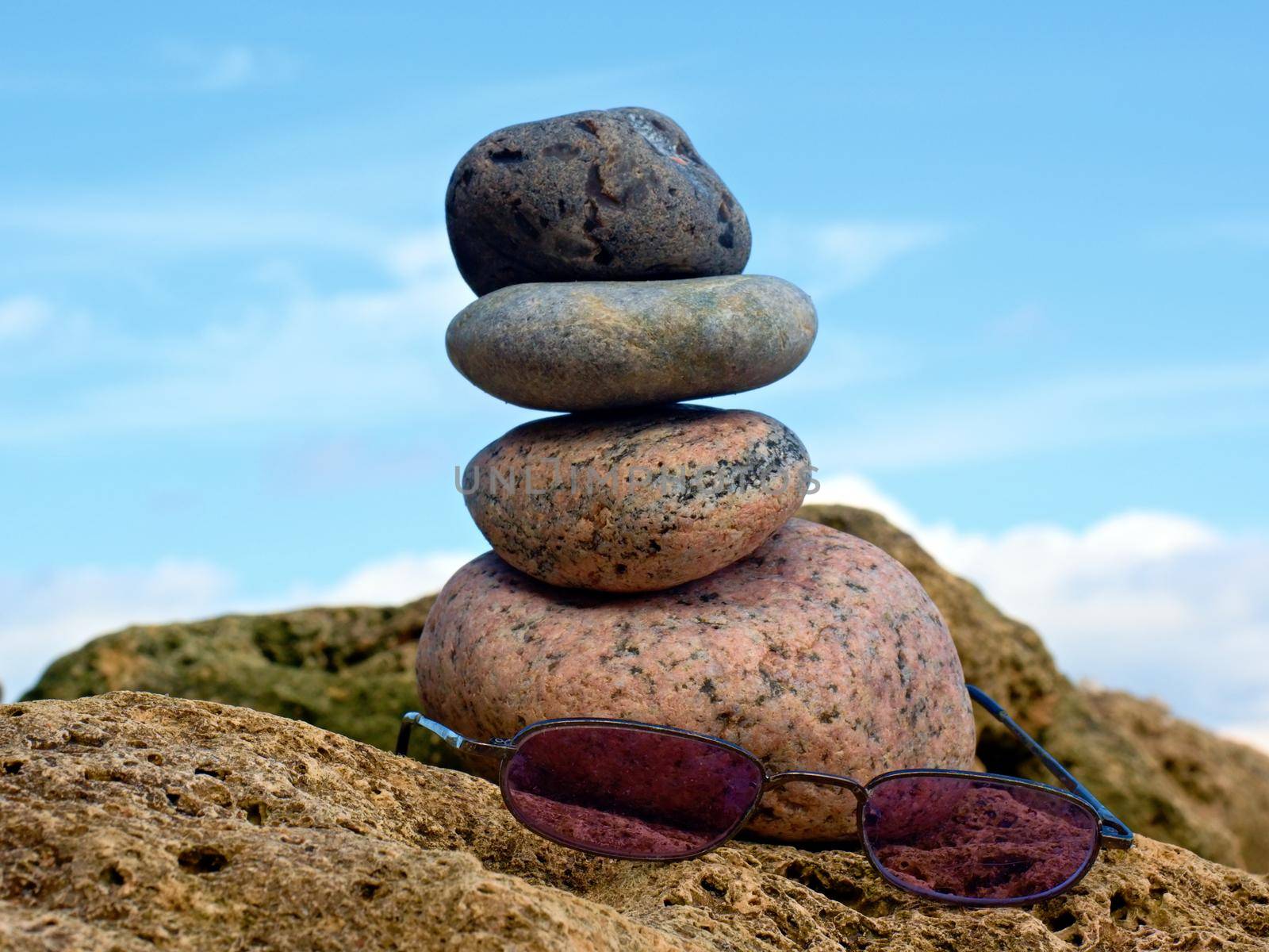 Pink summer glasses and stone pyramid on sea shore, waves in background. 