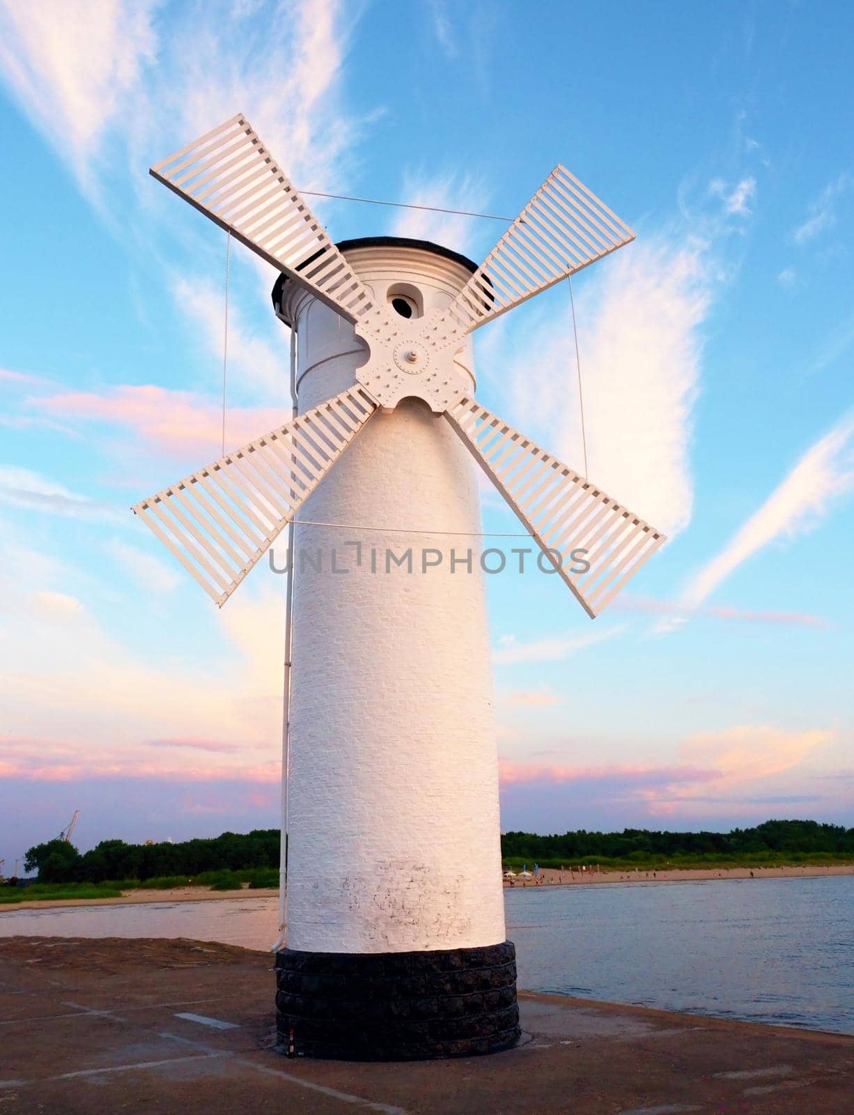 White old lighthouse decorated as windmill by sea on rocky coast. Seascape and landscape in background