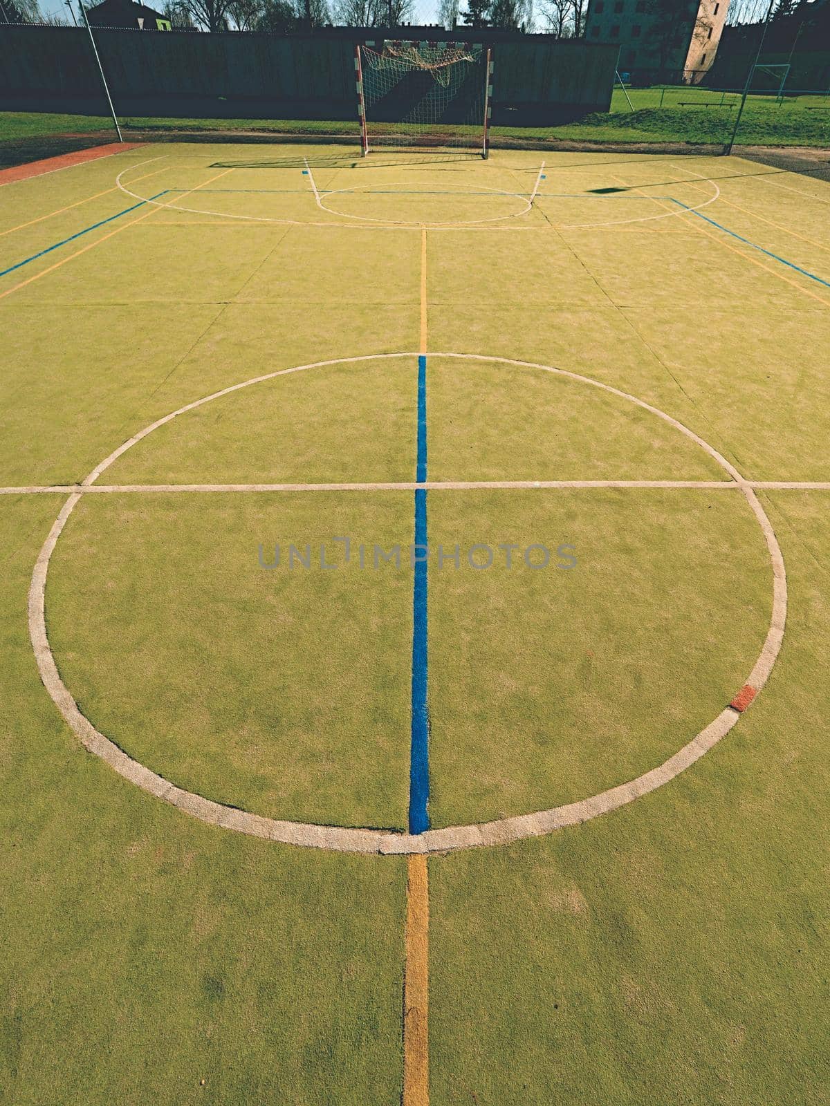 Empty outdoor handball playground, plastic hairy green surface on ground and white blue bounds lines. 