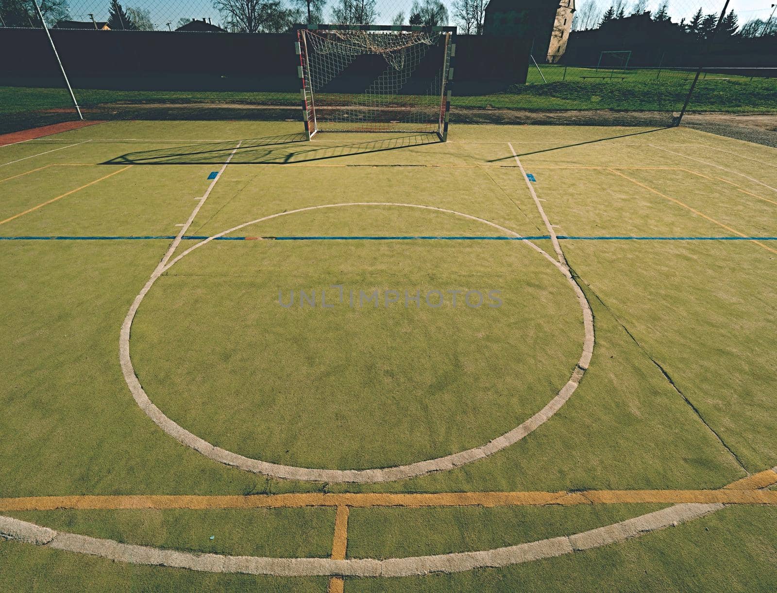 Empty outdoor handball playground, plastic hairy green surface on ground and white blue bounds lines. 