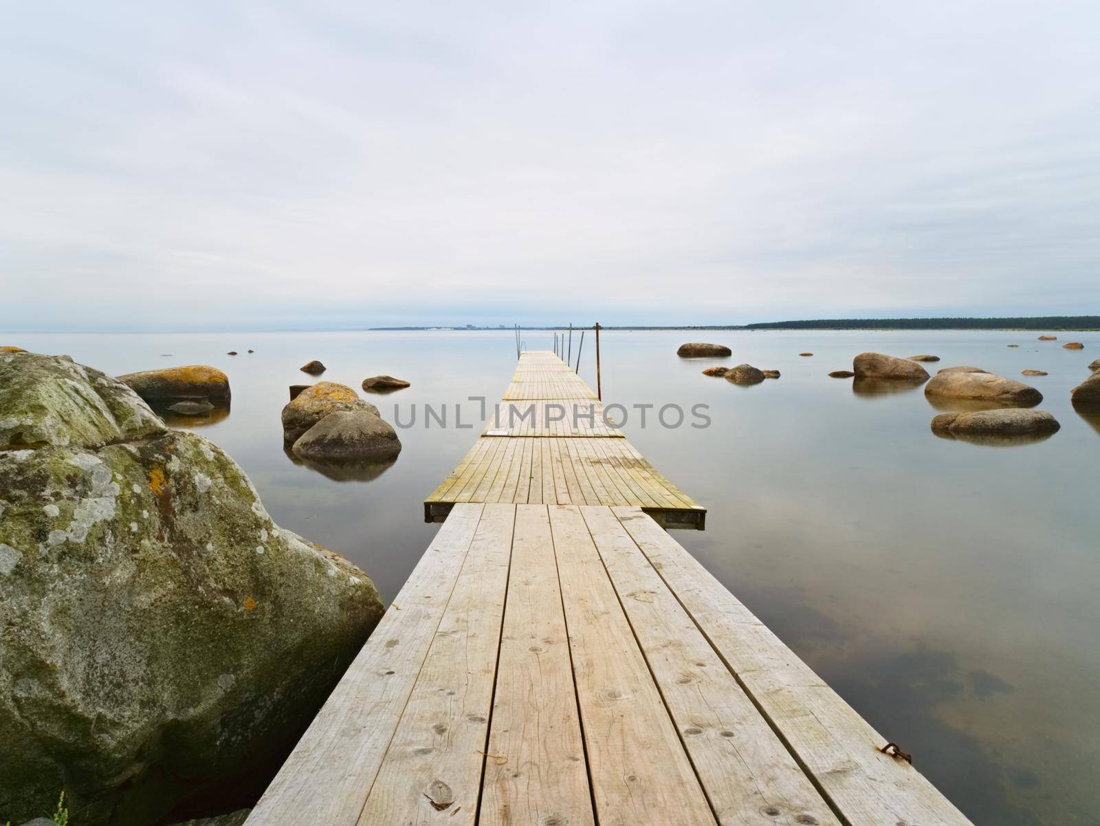 Empty wooden mole in water of blue lake.  Old fishing wharf for hired boats and swimmers. Waves smooth by long exposure, cloudy sky.