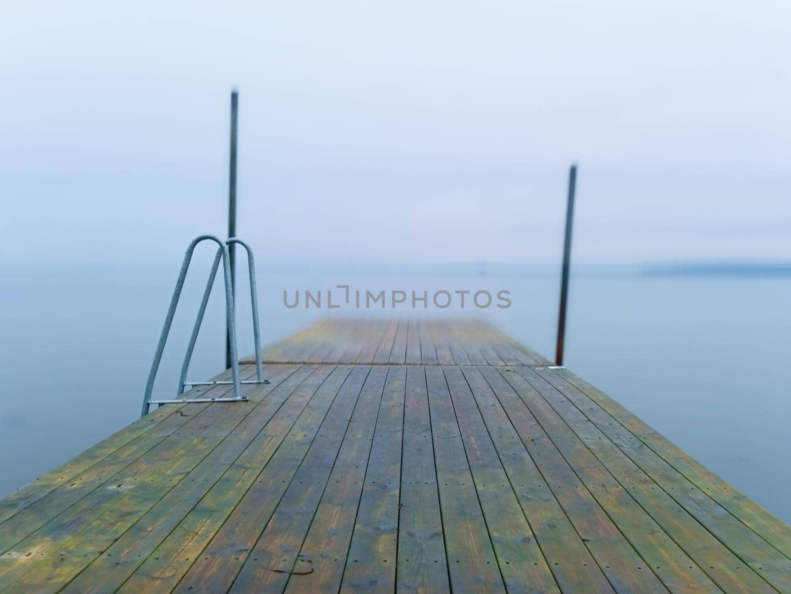 Abandoned wooden wharf mole in sea within sunrise. Gentle blue pink color of sky blurry waves on water level.