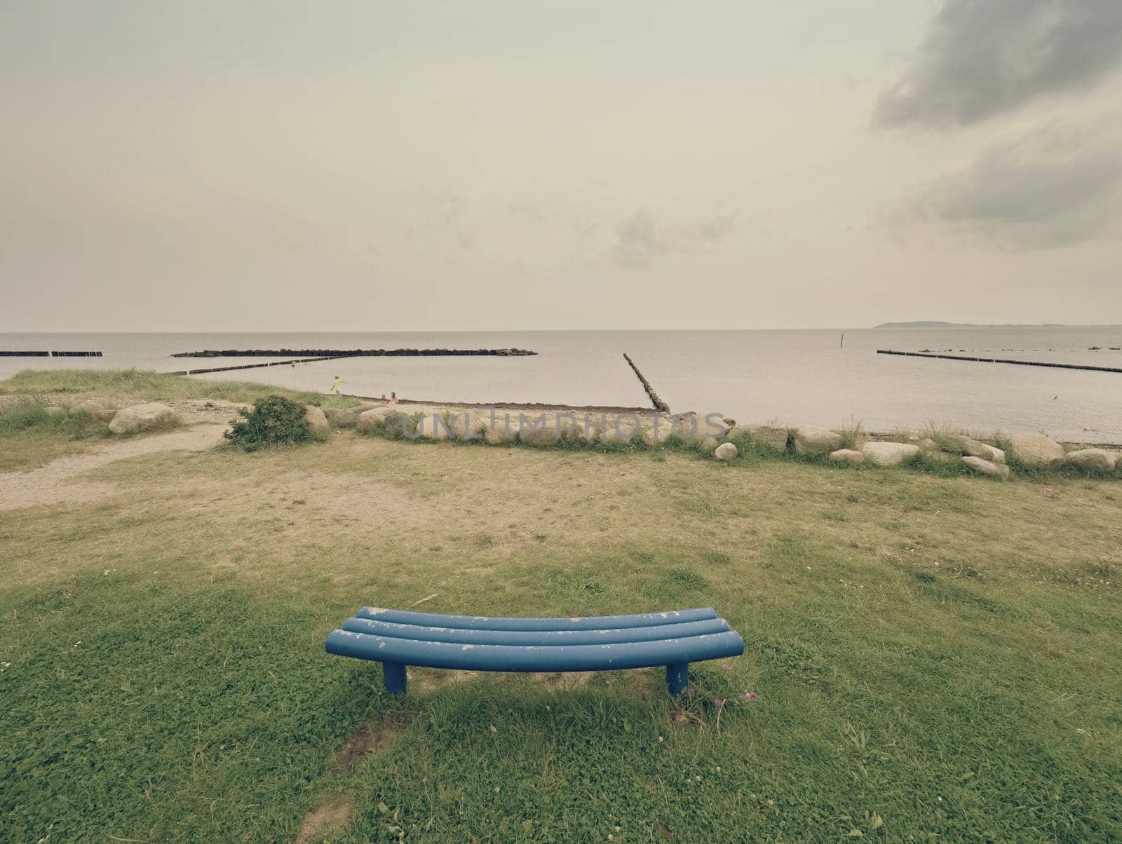 Stony beach and blue bench. Bench by the sea in the cloudy sunrise