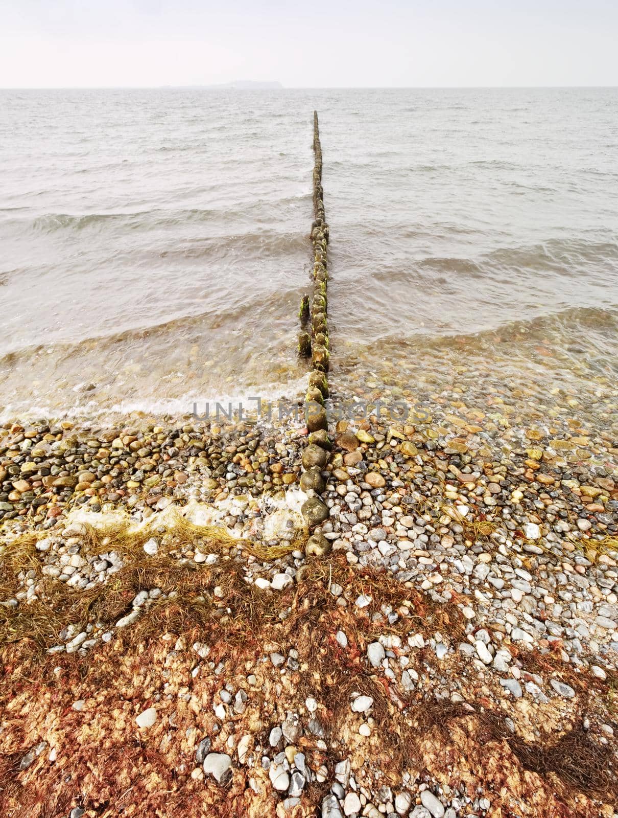 Wooden breakwater in wavy Baltic Sea. Evening at smooth wavy sea. Low clouds by rdonar2