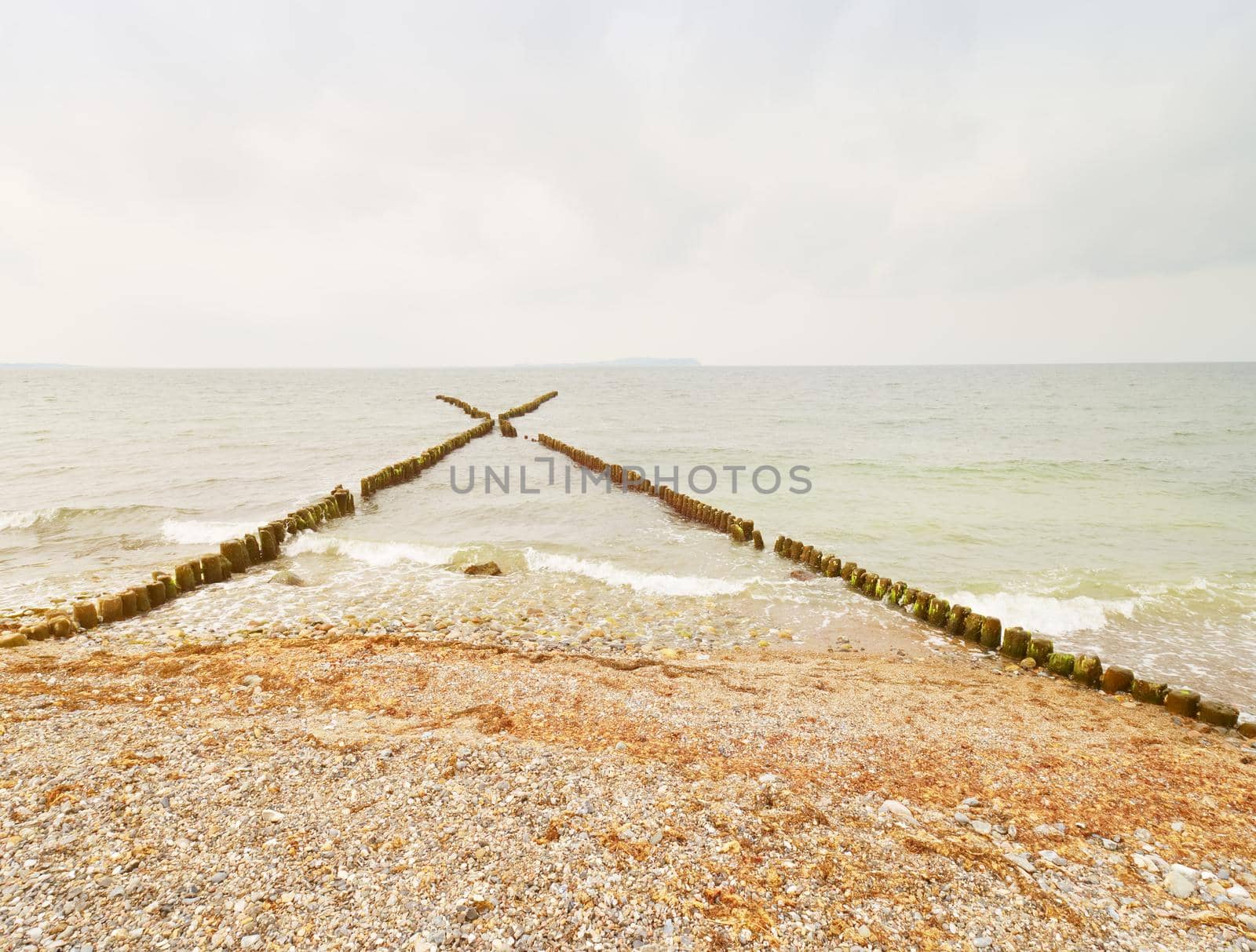 Old wooden breakwaters on a shore of Baltic Sea. White foamy water splashing stones  by rdonar2