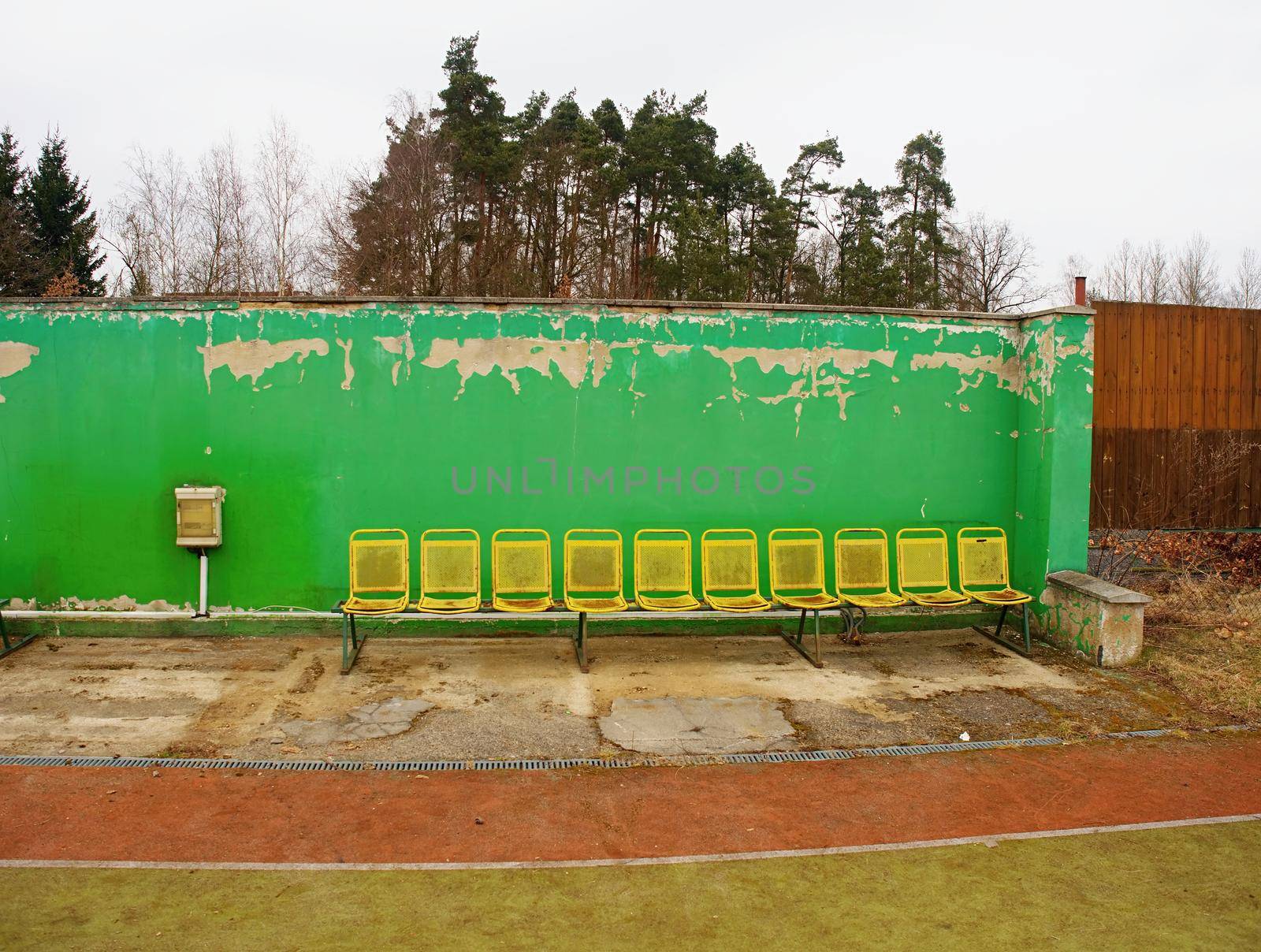 Old yellow rusty metal seats on outdoor stadium. Players bench chairs with poor paint 