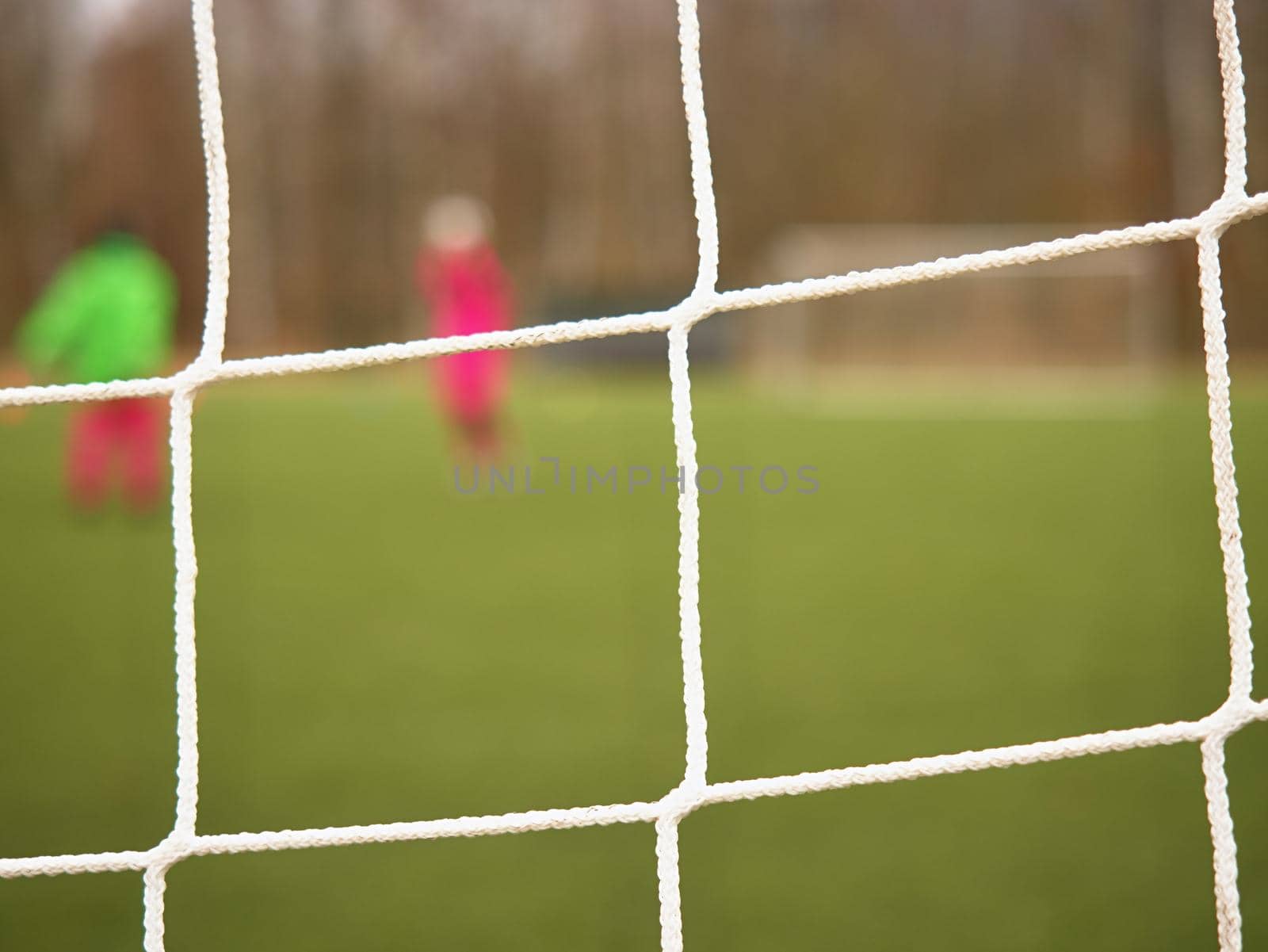 Football player stands against goal with net and stadium. Football gate net. Soccer gate net.  In blurry background stand people.