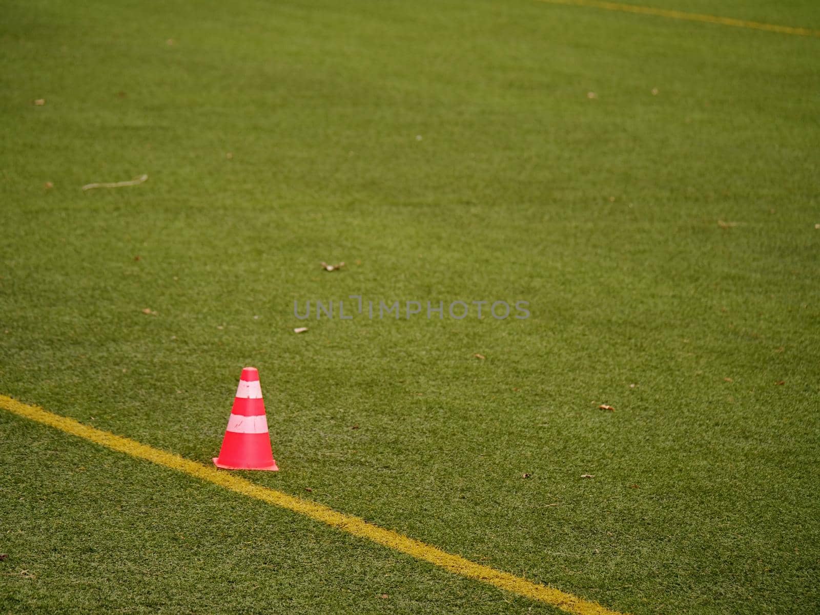 Bright red plastic cone on painted white line of soccer field. Football green playground with  rubber cone