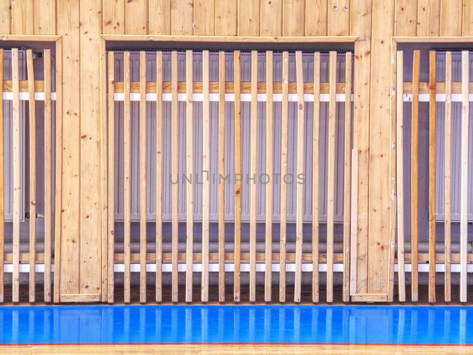 Heating radiator on wall with wooden ribs row cover, construction of wooden bars.  Painted wooden floor of sports hall with colorful marking lines. Schooll gym hall