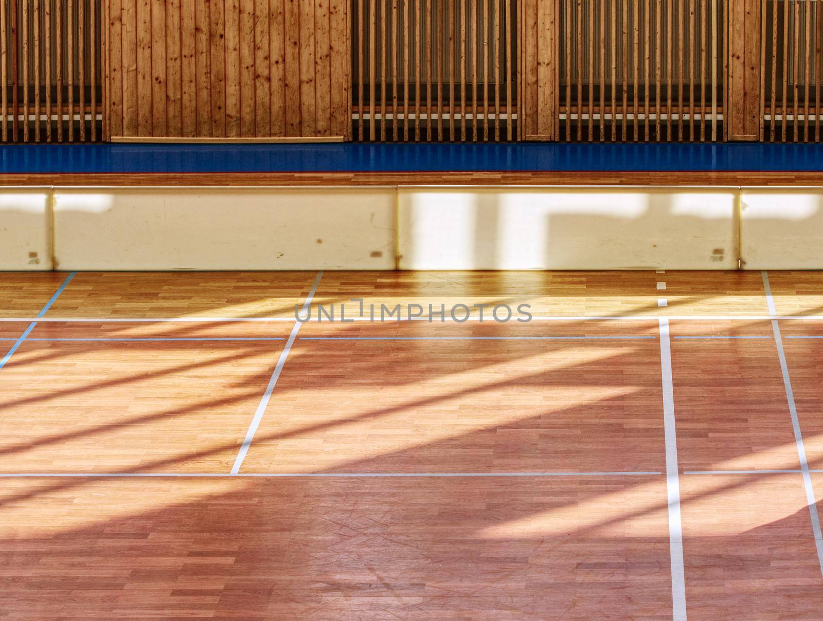 Schooll gym hall with water heating system hidden over wooden bars cover.  Basketball court. Lines of playfield in hall.