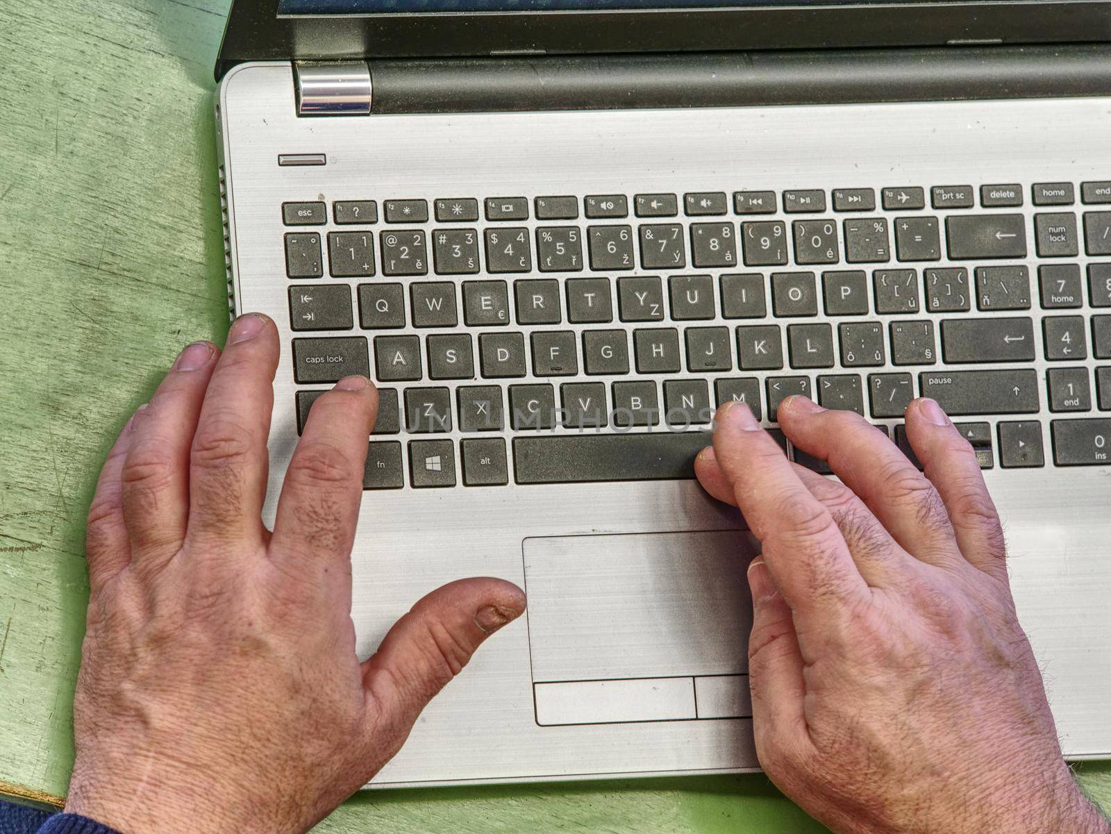 Hands of an elderly person on a laptop keyboard. Grandfather works behind laptop, typing on keyboard with her old hands with wrinkles.