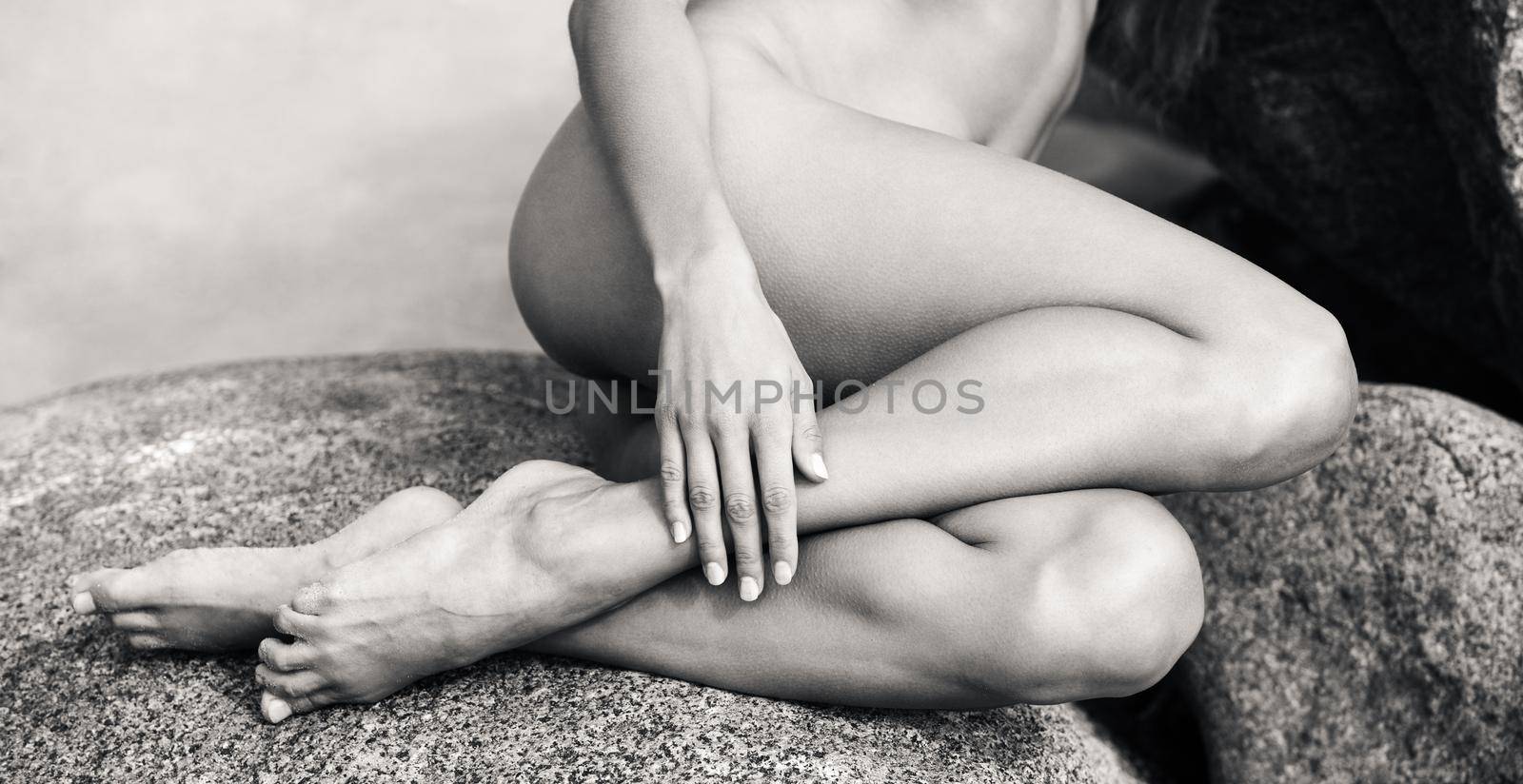 Black and white image of beautiful young nude woman sitting on the stones