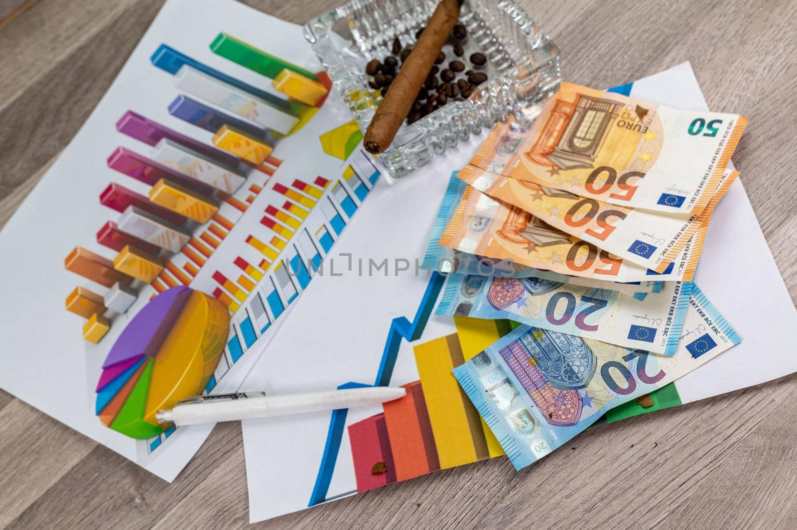 wooden table with 50 and 20 euro banknotes ashtray and cigar with statistics and pen