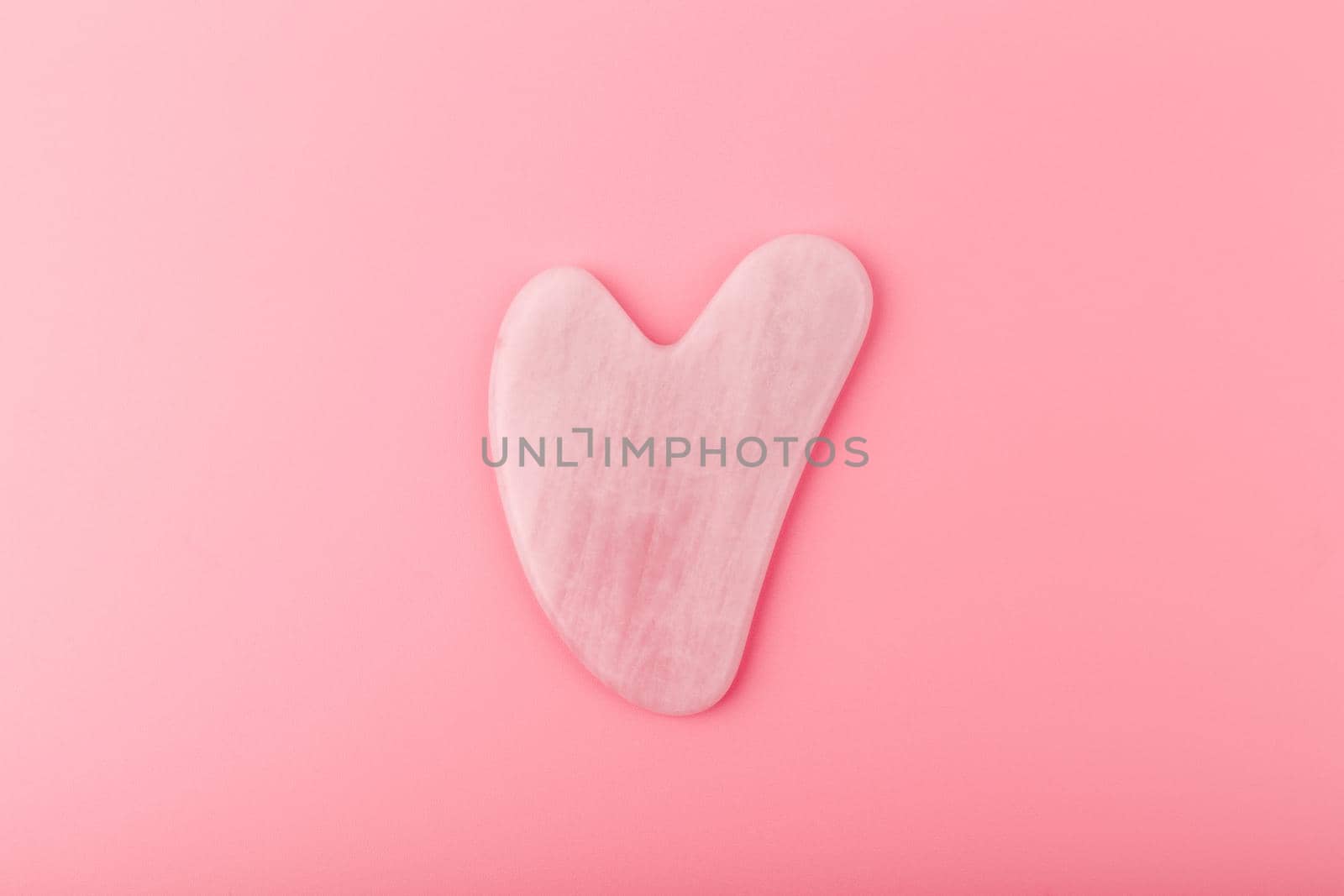 Top view of pink heart shaped guasha stone made of quartz crystal on bright pink background. Concept of alternative skin care treatment, self massage and acupressure