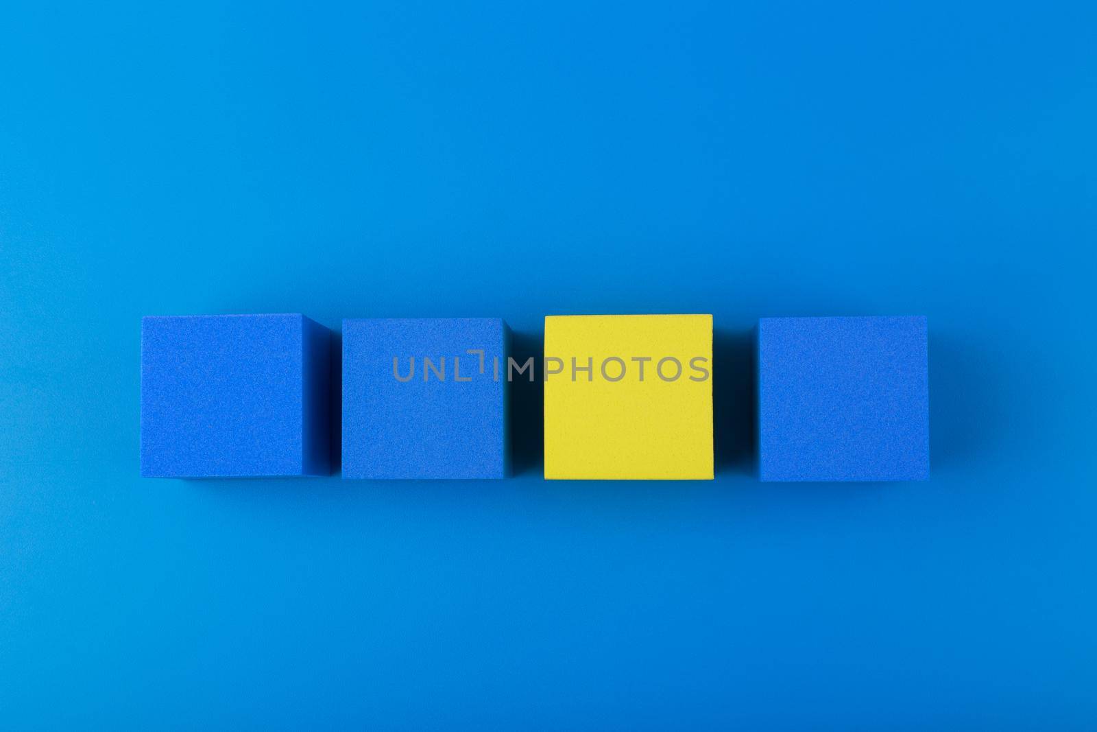 Creative flat lay with three blue and one yellow blocks in a row against blue background. Concept of individuality and identity