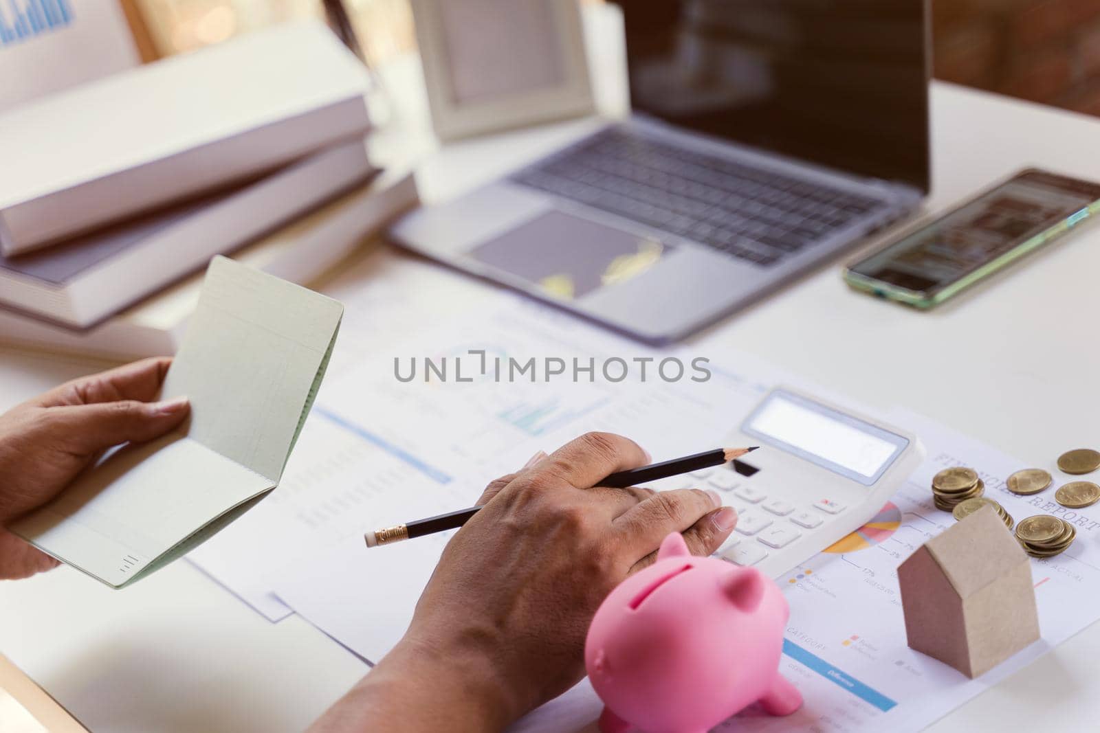 Business owner checking saving account passbook and using a calculator with money coin, piggy bank, laptop, budget and income document. Business saving finance concept.