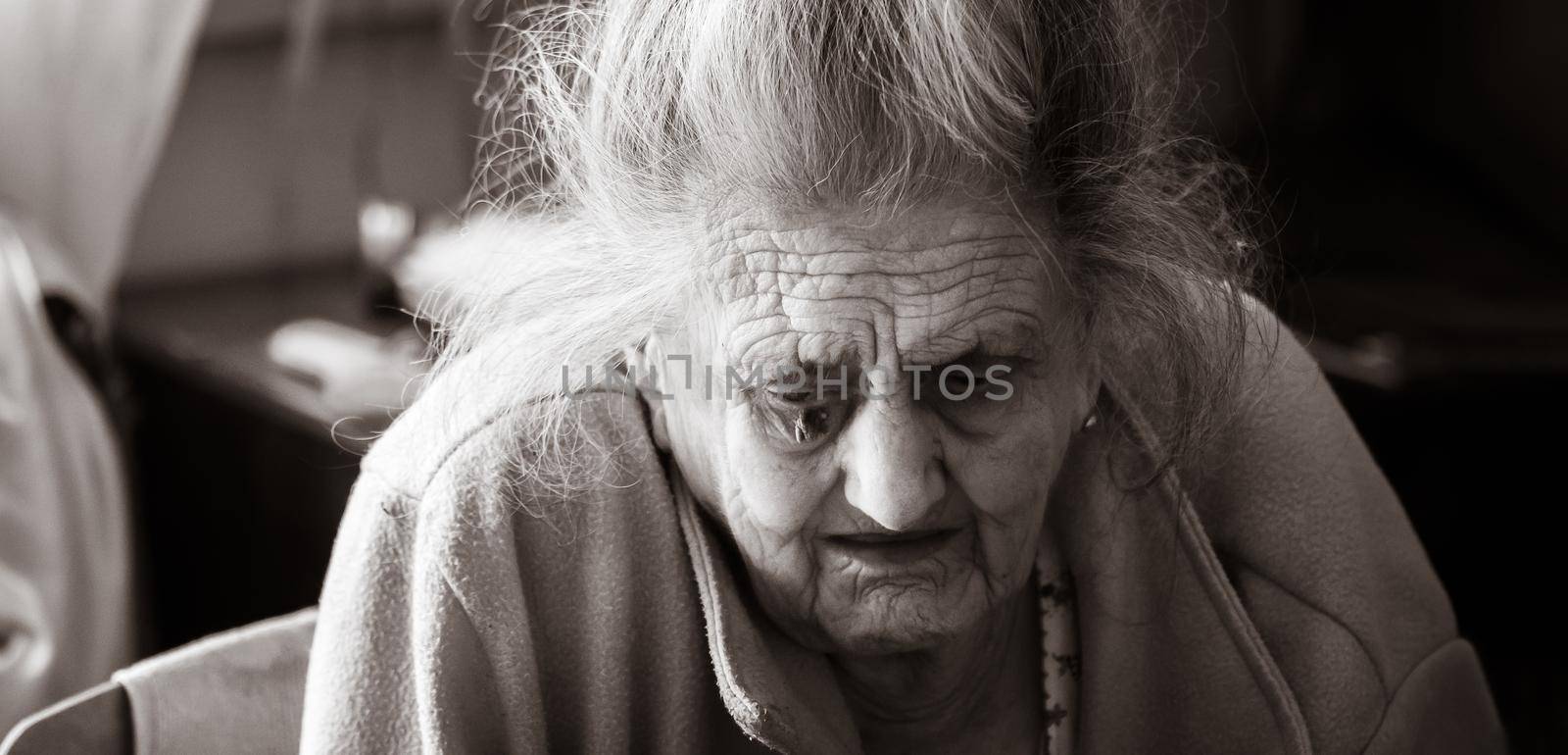 Old age concept. Portrait of a very old and tired of life wrinkled woman near the window in the bedroom of her house. Sad and depressed older woman alone