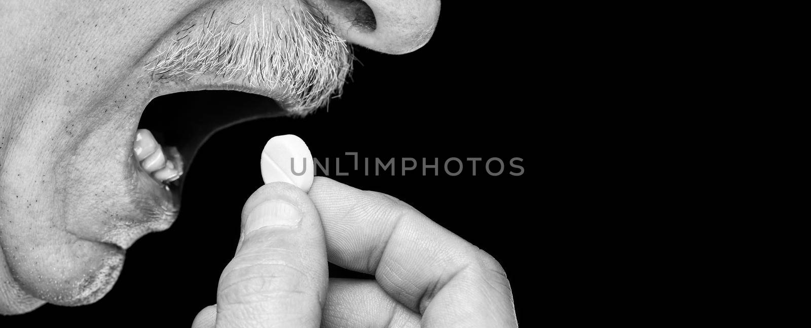 Health care concept. Close-up black and white image of an old man wants to take a pill isolated on black background with copy-space
