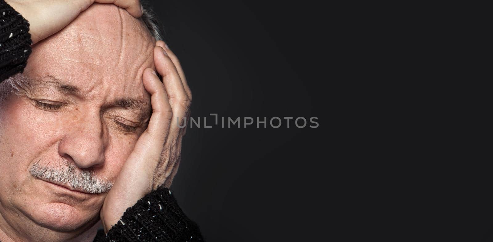 an older man suffering from a headache on dark background
