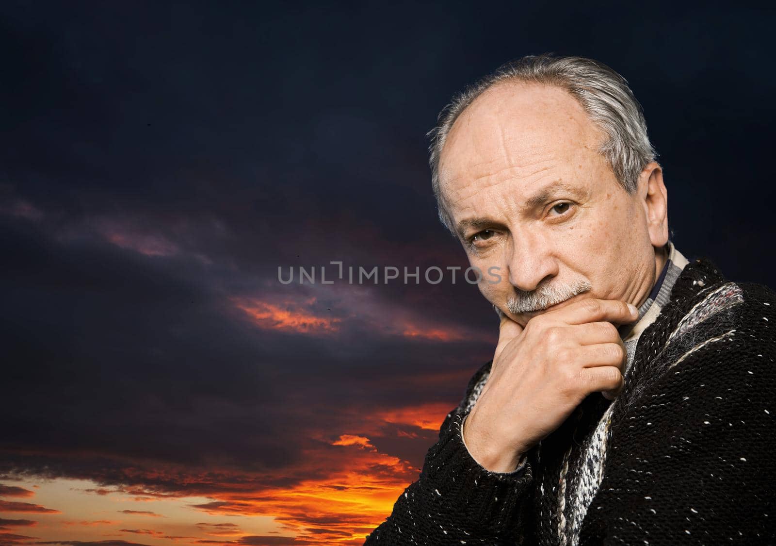 Portrait of handsome senior man prop up the head with his hand on sunset sky background