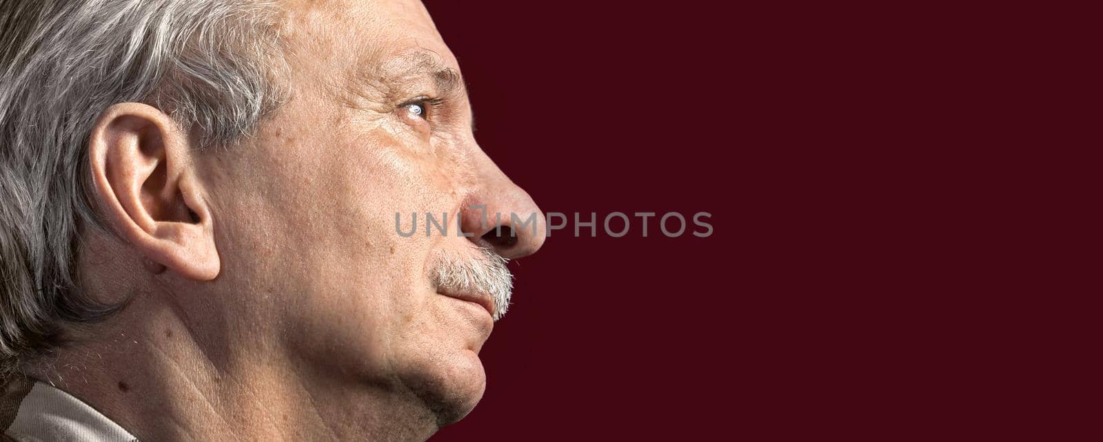 Portrait of handsome senior man with a tired expression on dark red background with copy-space