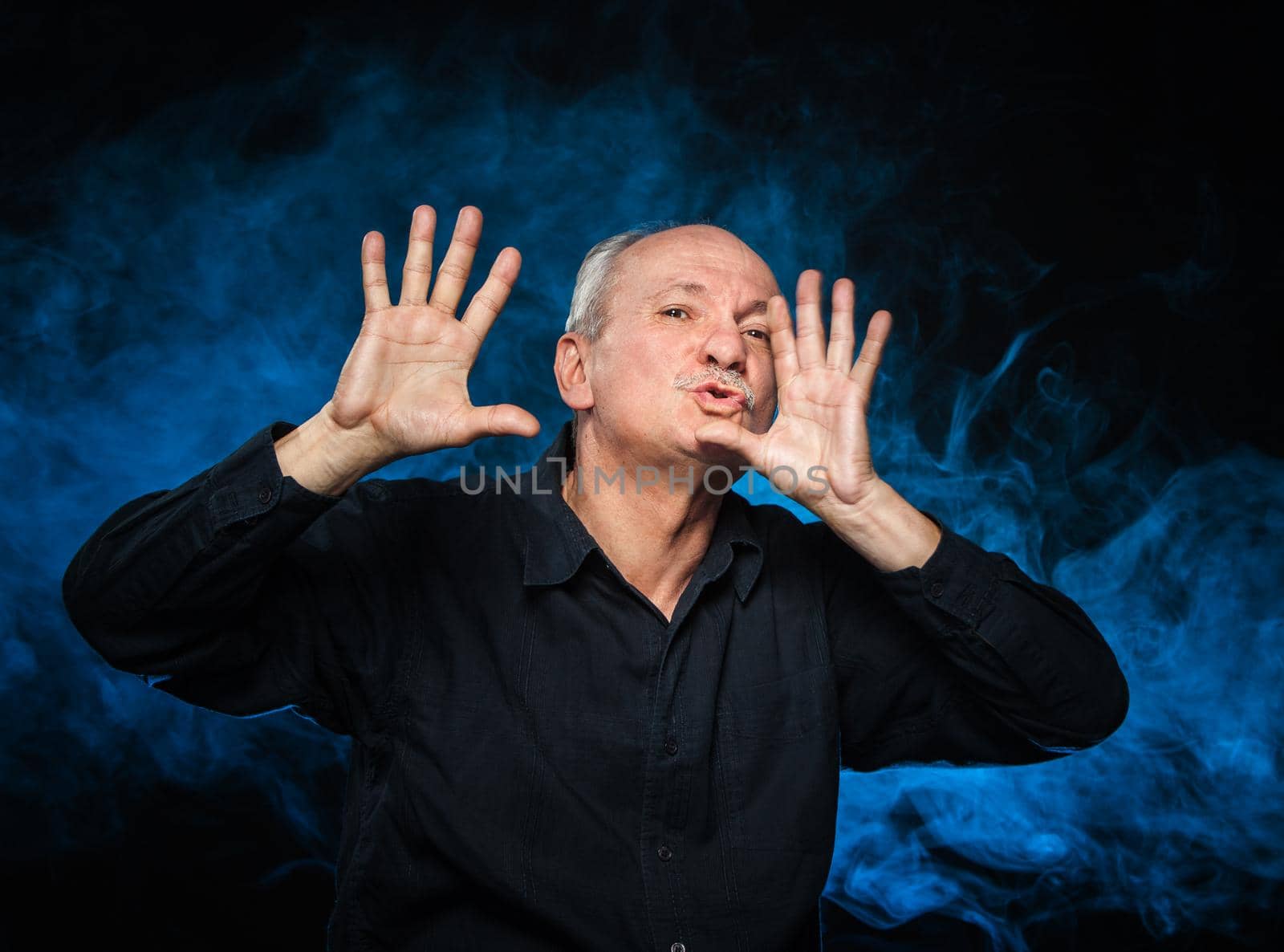 Happy elderly man gesturing on a dark background and blue smoke