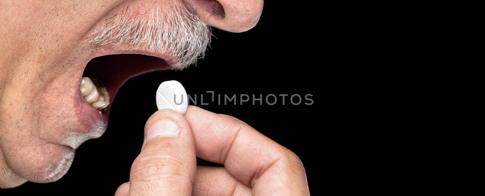 Close-up image of an old man wants to take a pill isolated on black background with copy-space