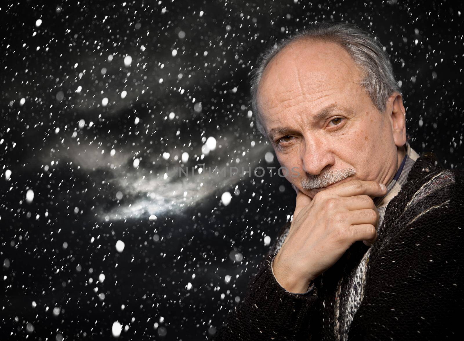 Portrait of an elderly man with a serious expression on a dark sky background during a snowfall