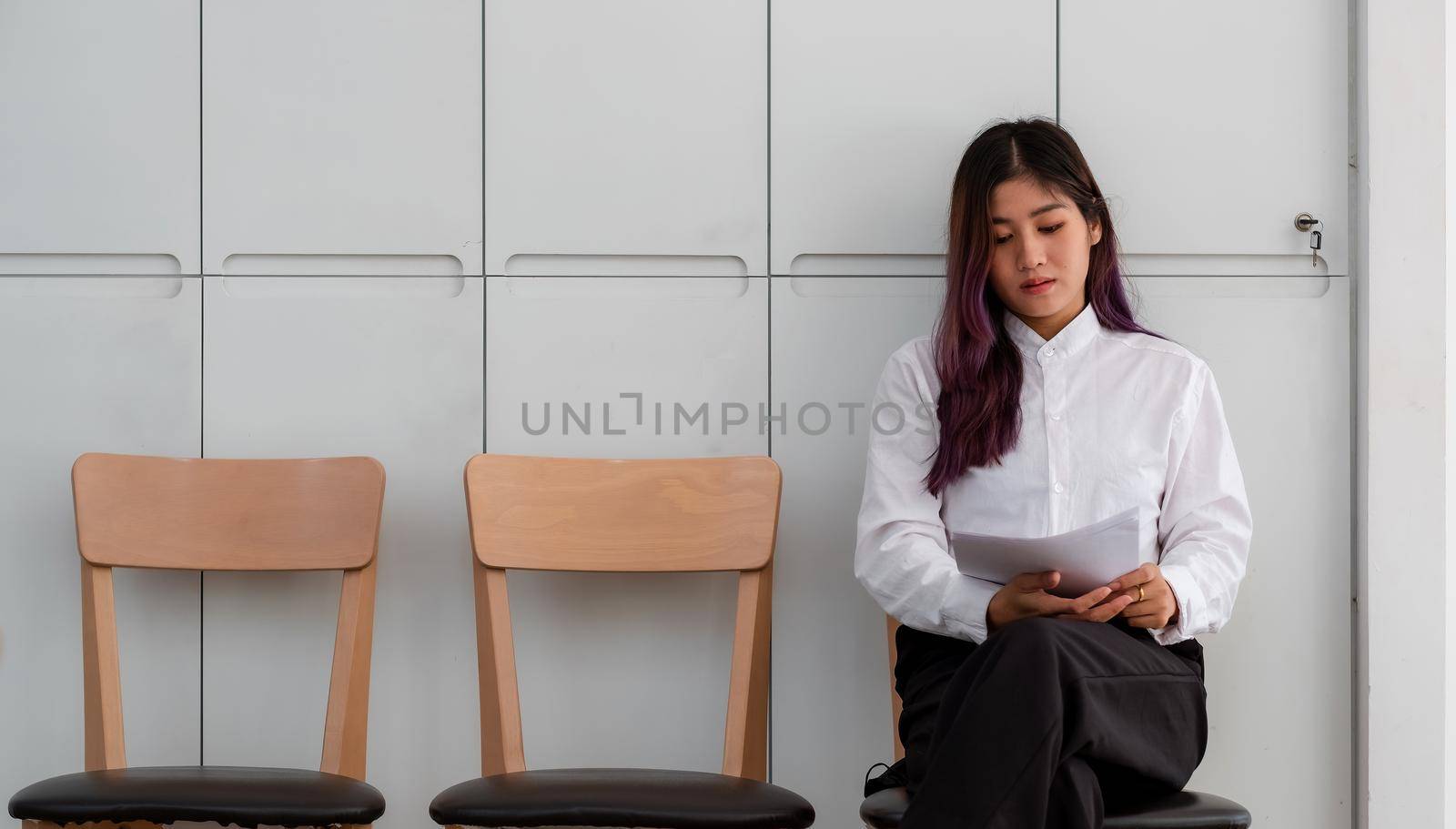 Asian woman with resume sitting to review the documents while waiting for a job interview.