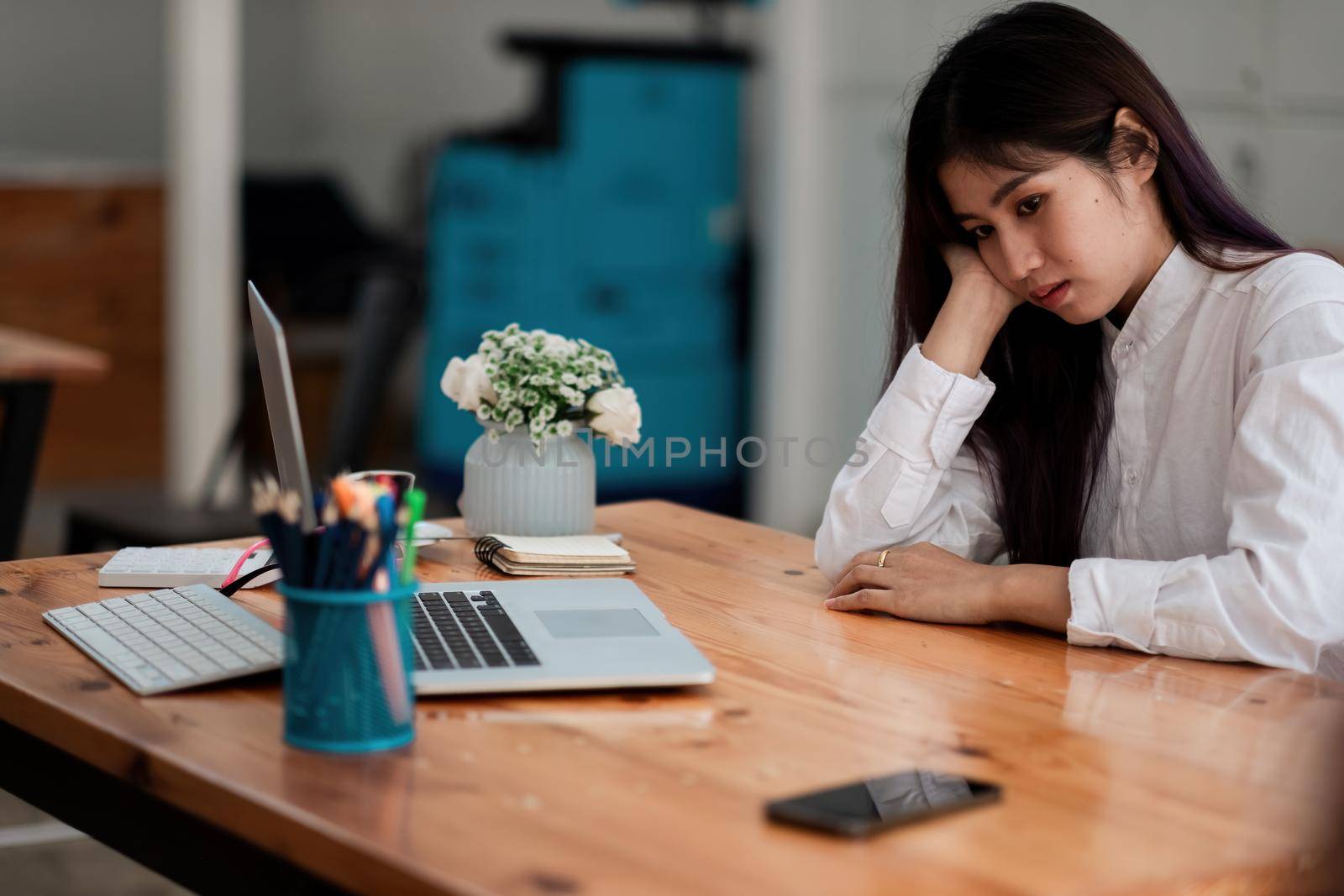 Bored asian female worker lie at office desk look at mobile phone and laptop screen think about problem solution, unmotivated businesswoman search inspiration, tired of monotonous work. Lack of motivation concept