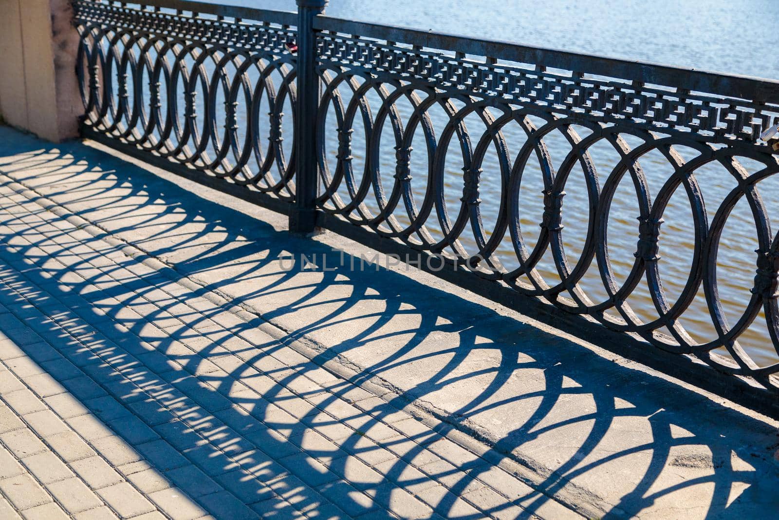 Shadows on a sunny day from the metal railings on the bridge over the river.