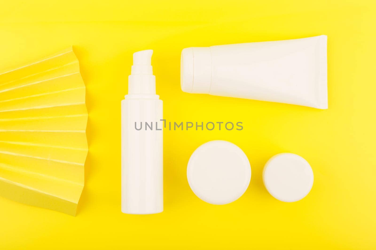 Creative flat lay with cosmetic products for skin care in white unbranded tubes on yellow background decorated with yellow waver. Concept of skin care and beauty treatment