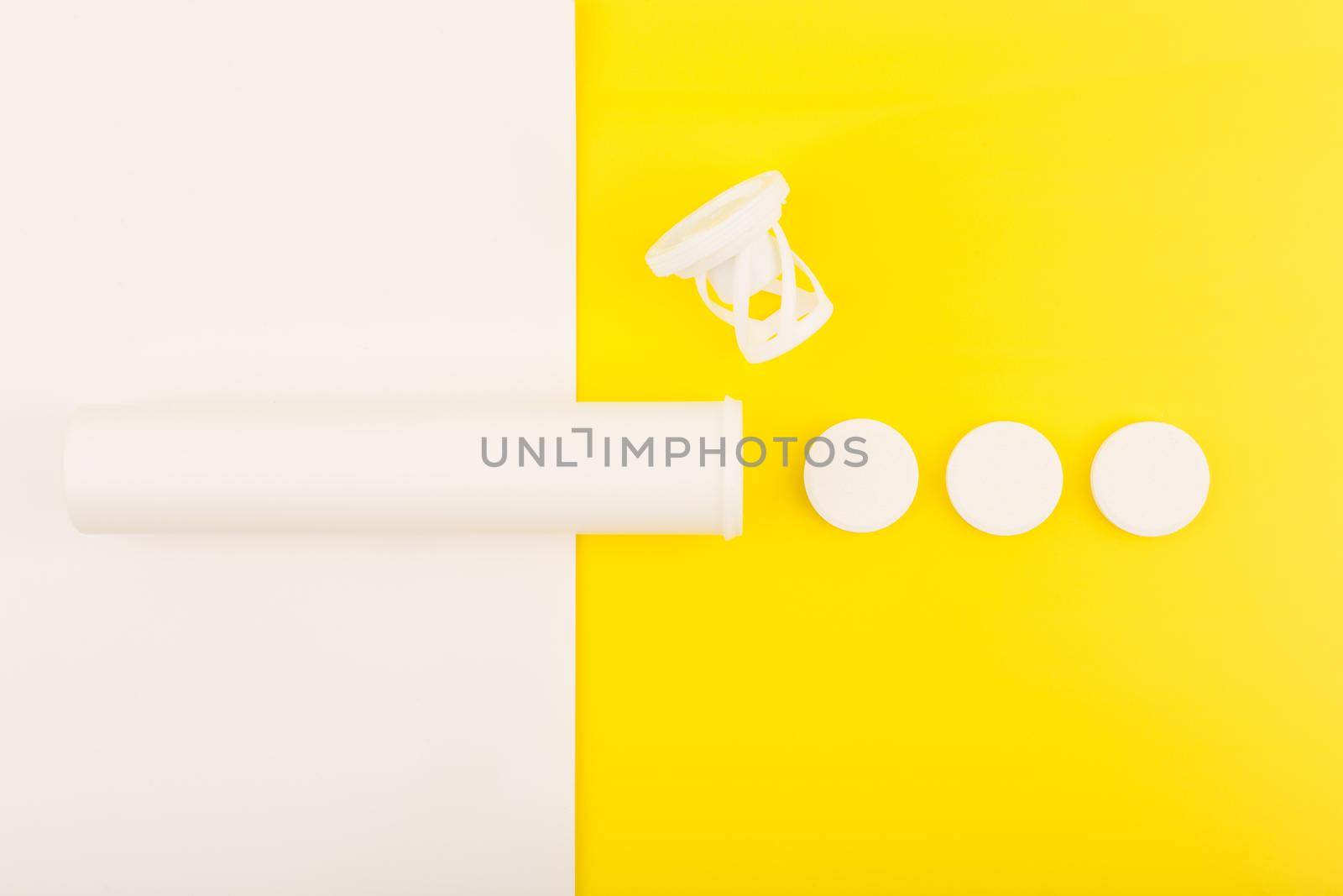 Creative simple flat lay with white opened tube with spilled effervescent vitamins on white and yellow background. Concept of vitamin C, supplements and healthcare