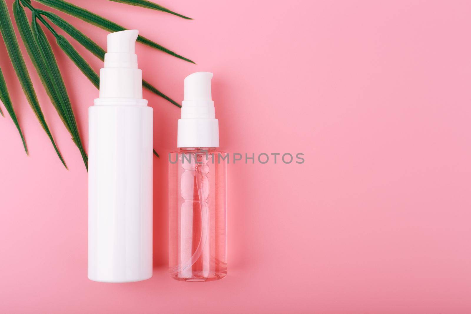 Creative flat lay with cosmetic set with face cream or lotion and pink cleansing foam in transparent bottle with dispenser on pink background with palm leaf and copy space. Concept of beauty products for daily skin care