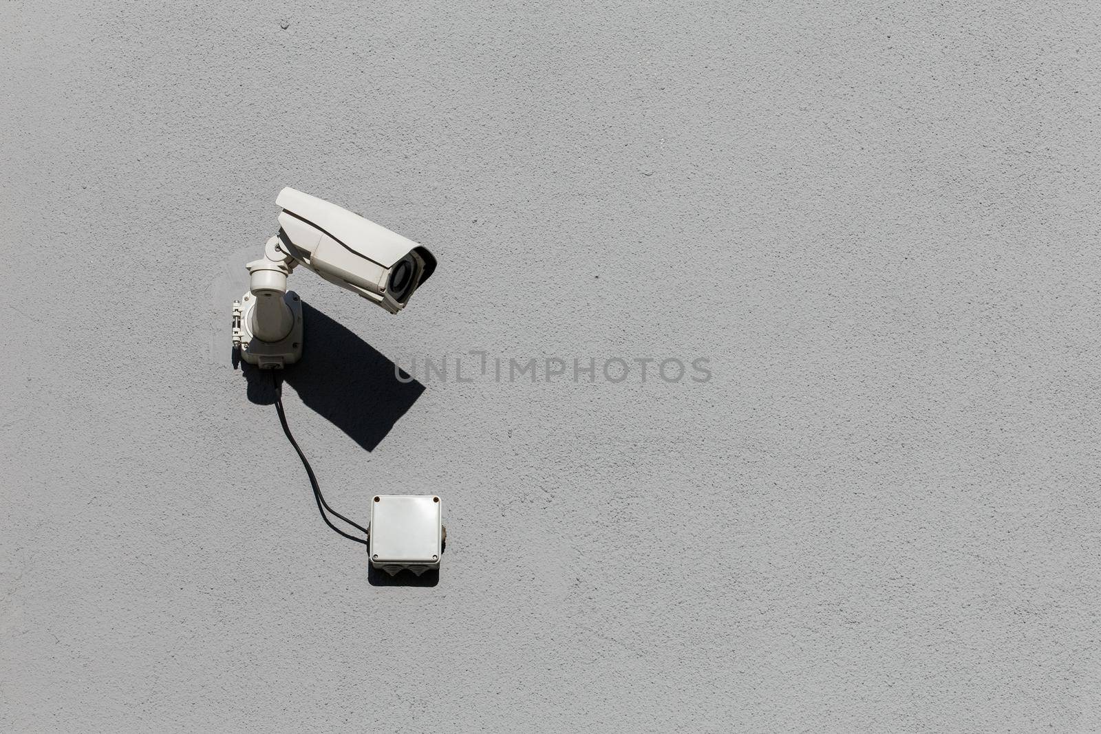 small white surveillance camera on flat gray matte plaster wall pointing sideways
