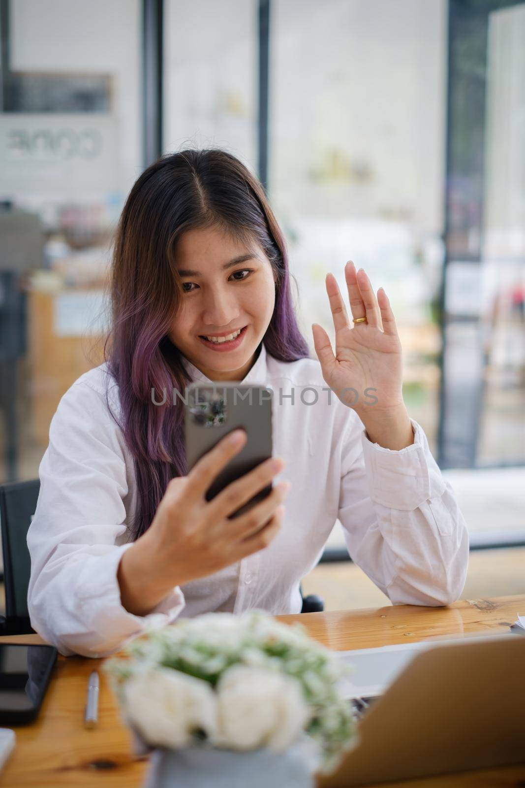 Joyful businesswoman sitting at desk looking at smartphone camera talking with friend make informal video call