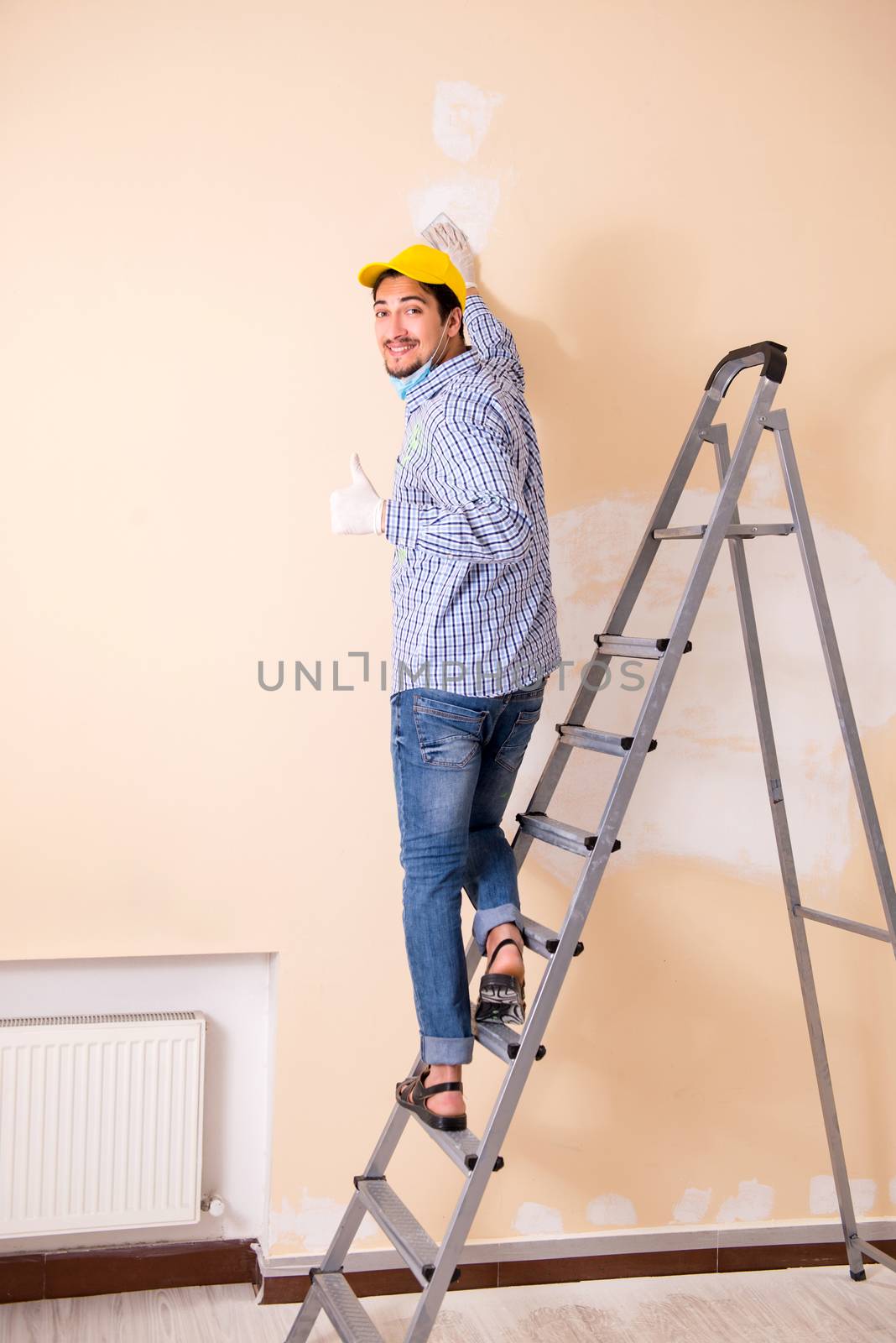 Young contractor sanding wall down with sandpaper 