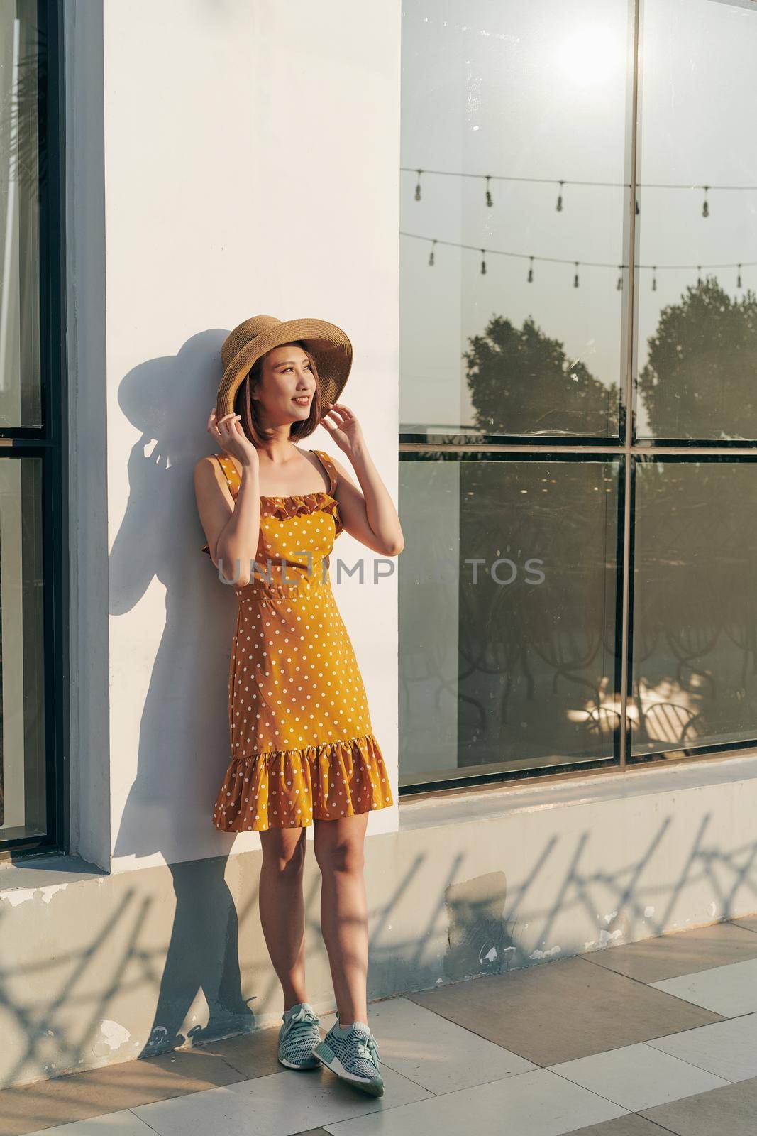 Summer sunny lifestyle fashion portrait of young Asia woman wearing hat and yellow dress by makidotvn