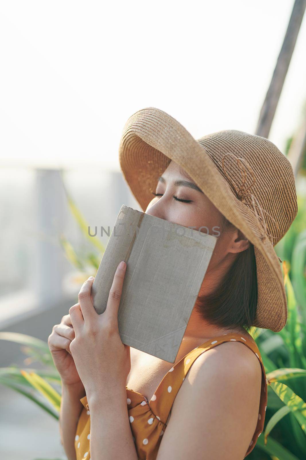 A girl closing eyes and covering her pretty face with book