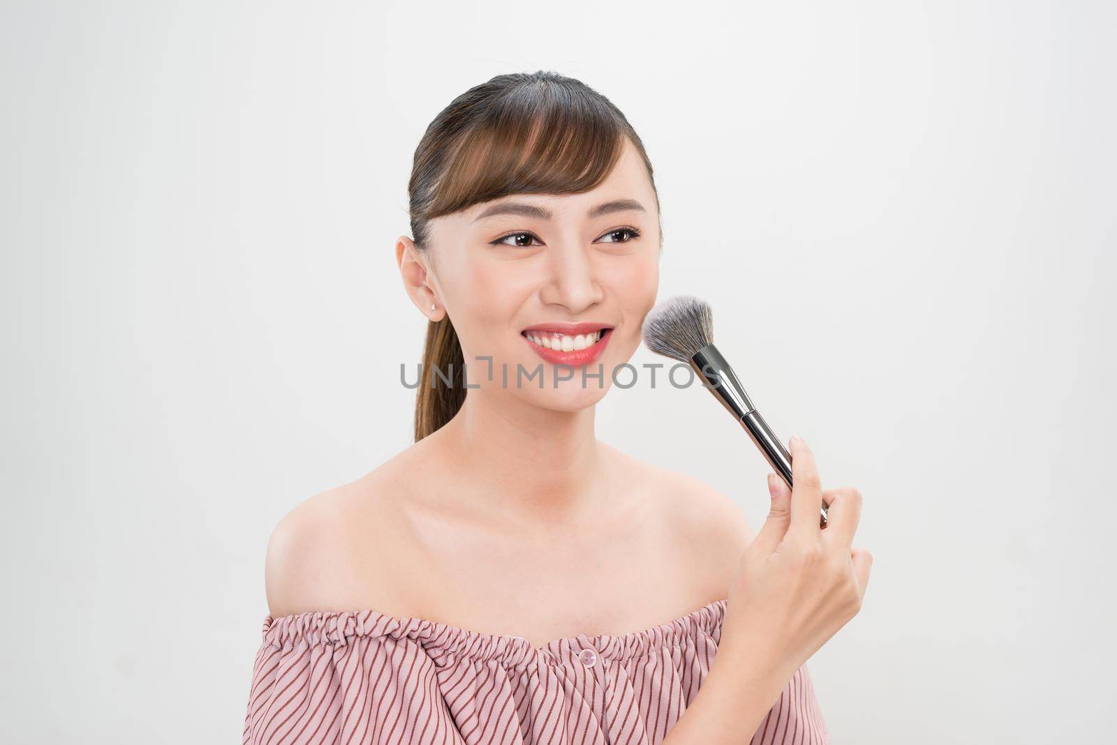 Beautiful smiling girl applying loose blush with cosmetic brush.